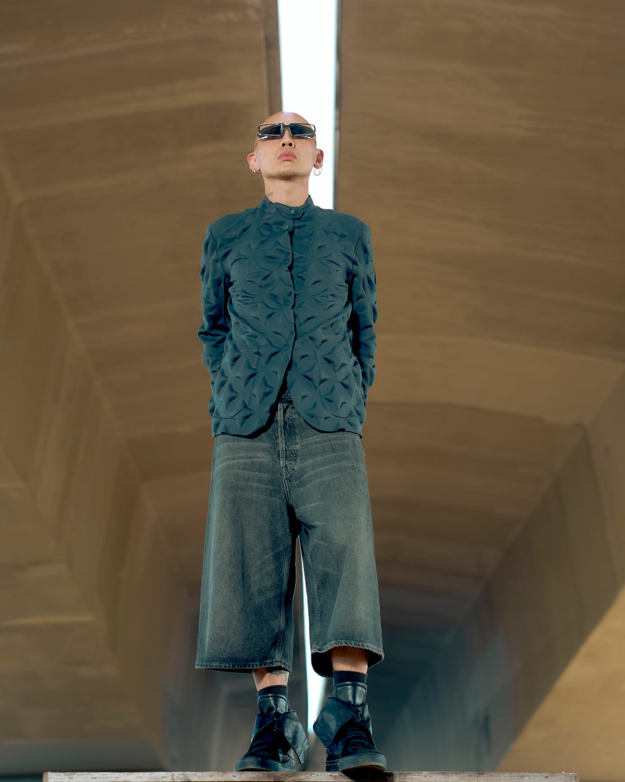 A person standing in an abstract, geometric space wearing a green Issey Miyake star-stamped jacket with a collarless design, patch pockets on hips, and press-stud front closures.