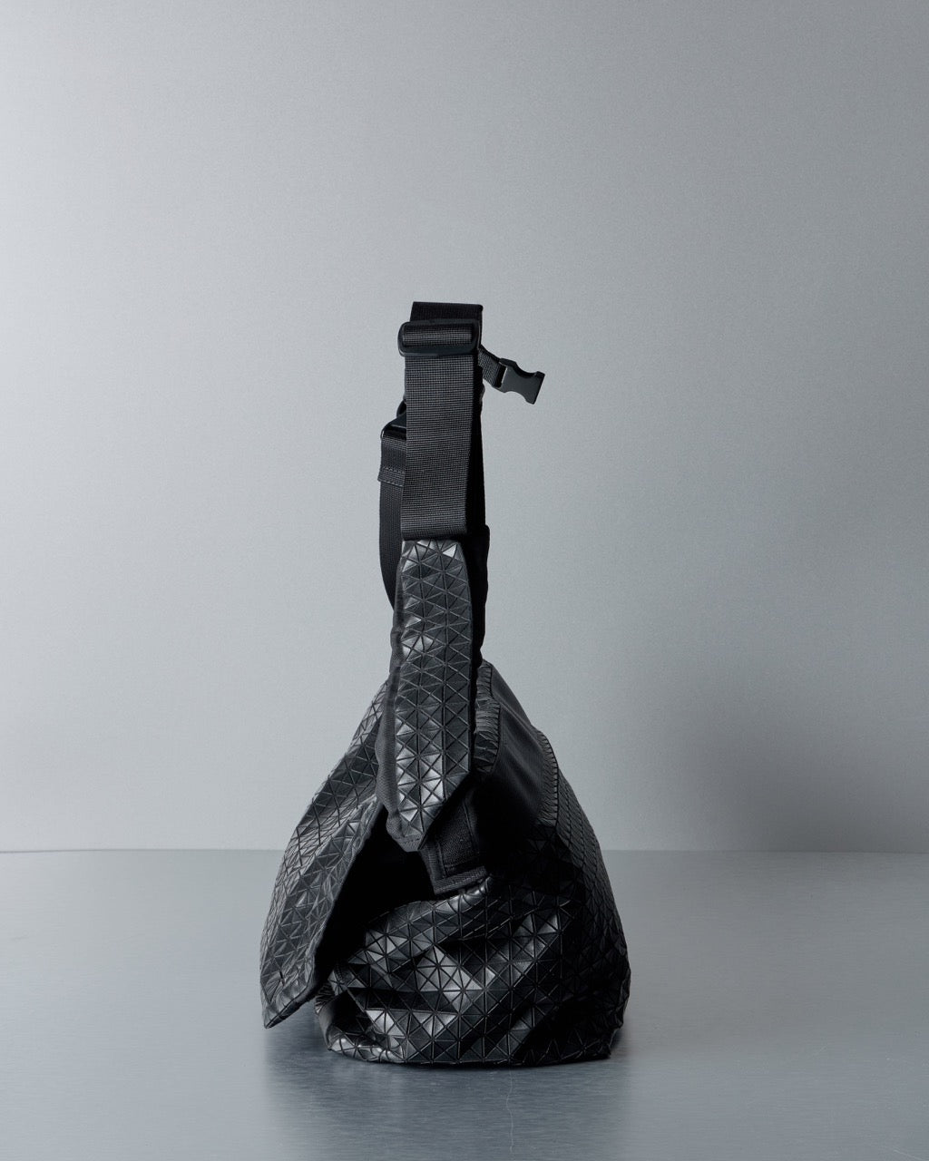 Black quilted Issey Miyake Bao Bao handbag on a gray background
