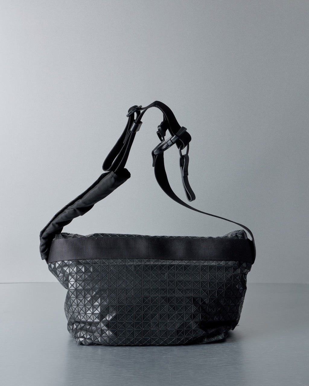 Black textured Issey Miyake Bao Bao handbag on a gray background