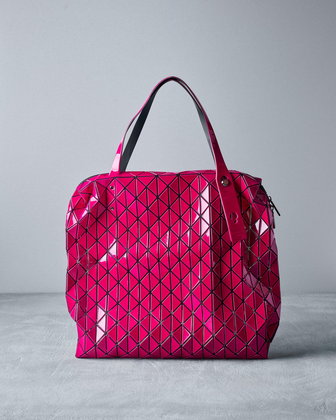 A bright pink Issey Miyake Bao Bao tote bag with a geometric pattern, featuring a top zip closure and polished metal hardware.