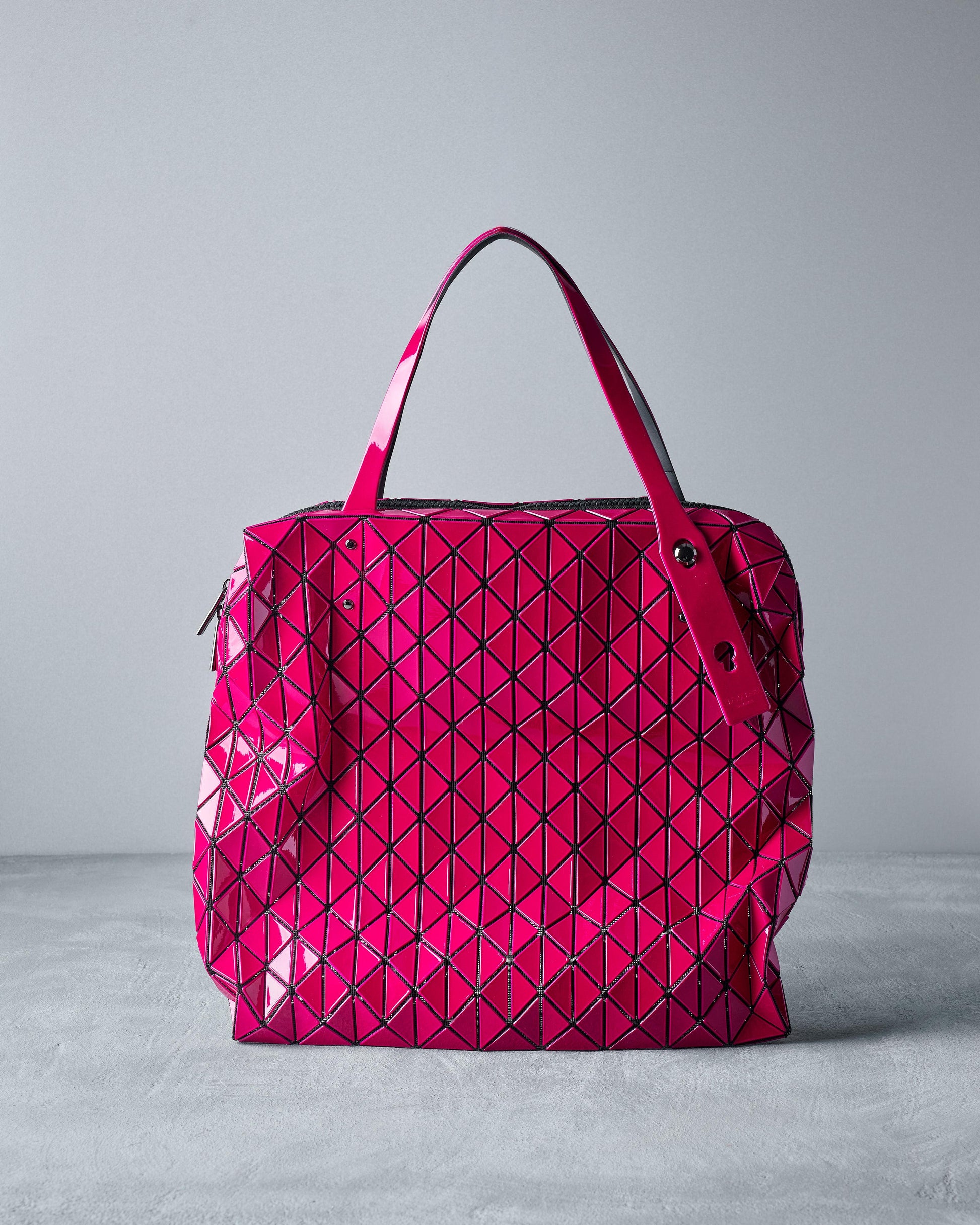 A bright pink Issey Miyake Bao Bao tote bag with a geometric pattern, featuring a top zip closure and polished metal hardware.