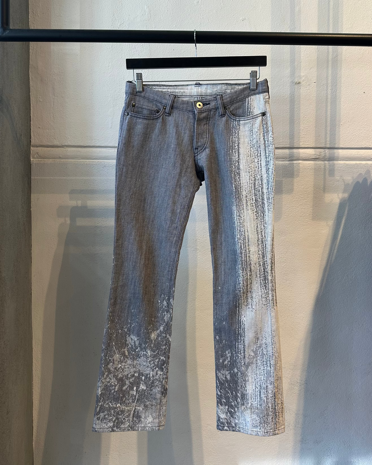 Distressed gray Issey Miyake jeans on a hanger against a reflective surface