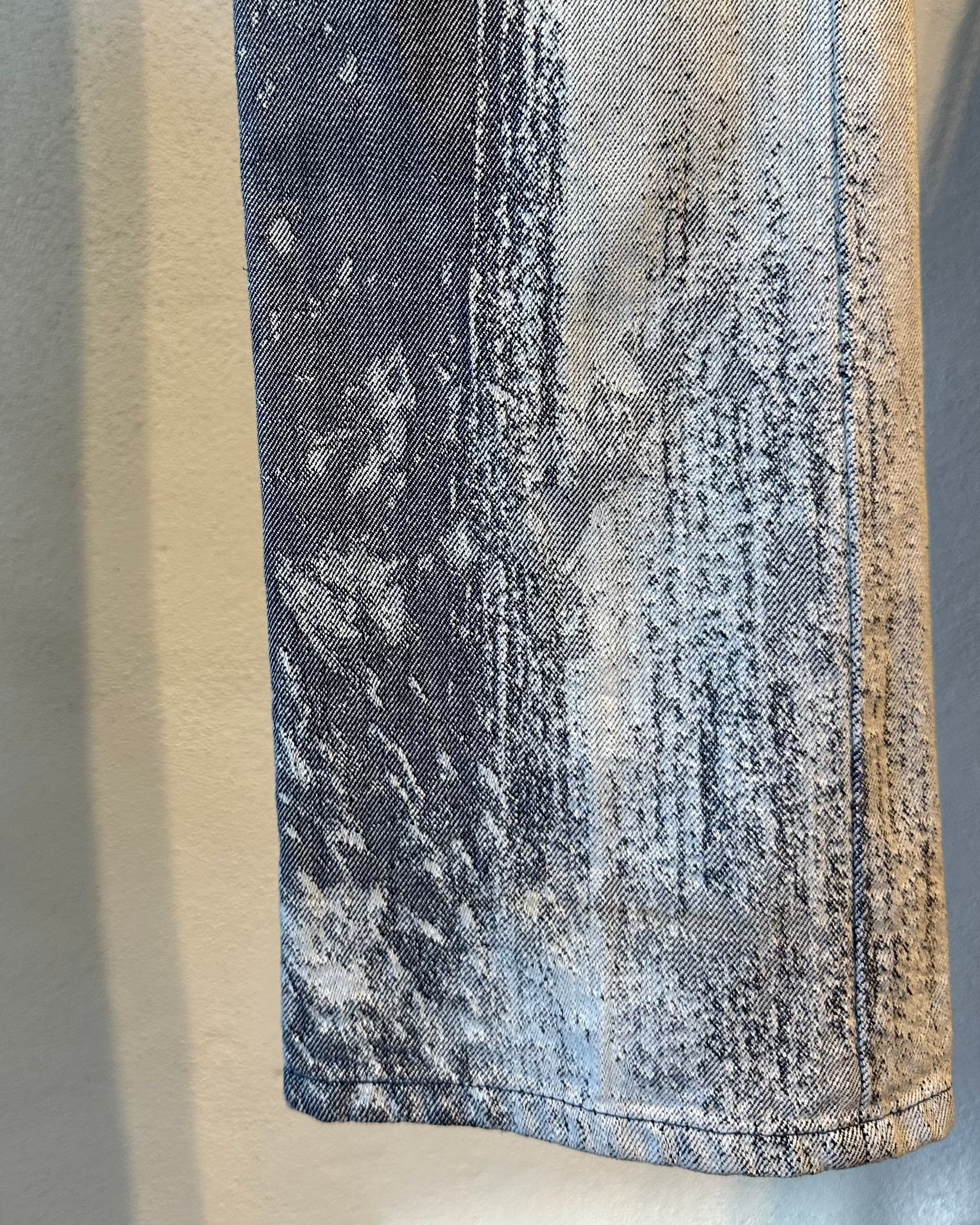 Close-up of a textured fabric on a pair of Issey Moiyake jeans with a gradient pattern on a neutral background