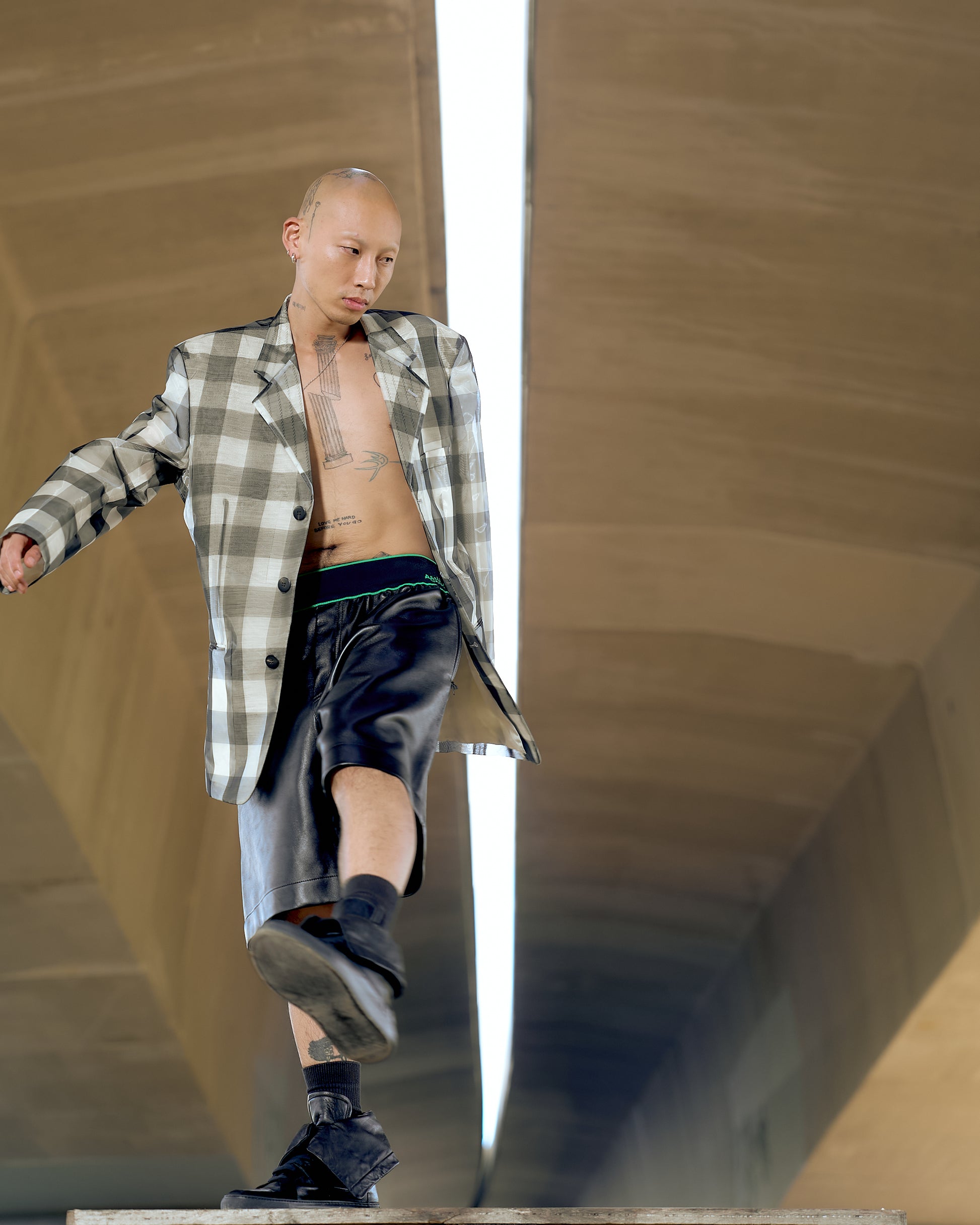 A person walks confidently in an oversized plaid Issey Miyake blazer and black shorts under a tunnel. 