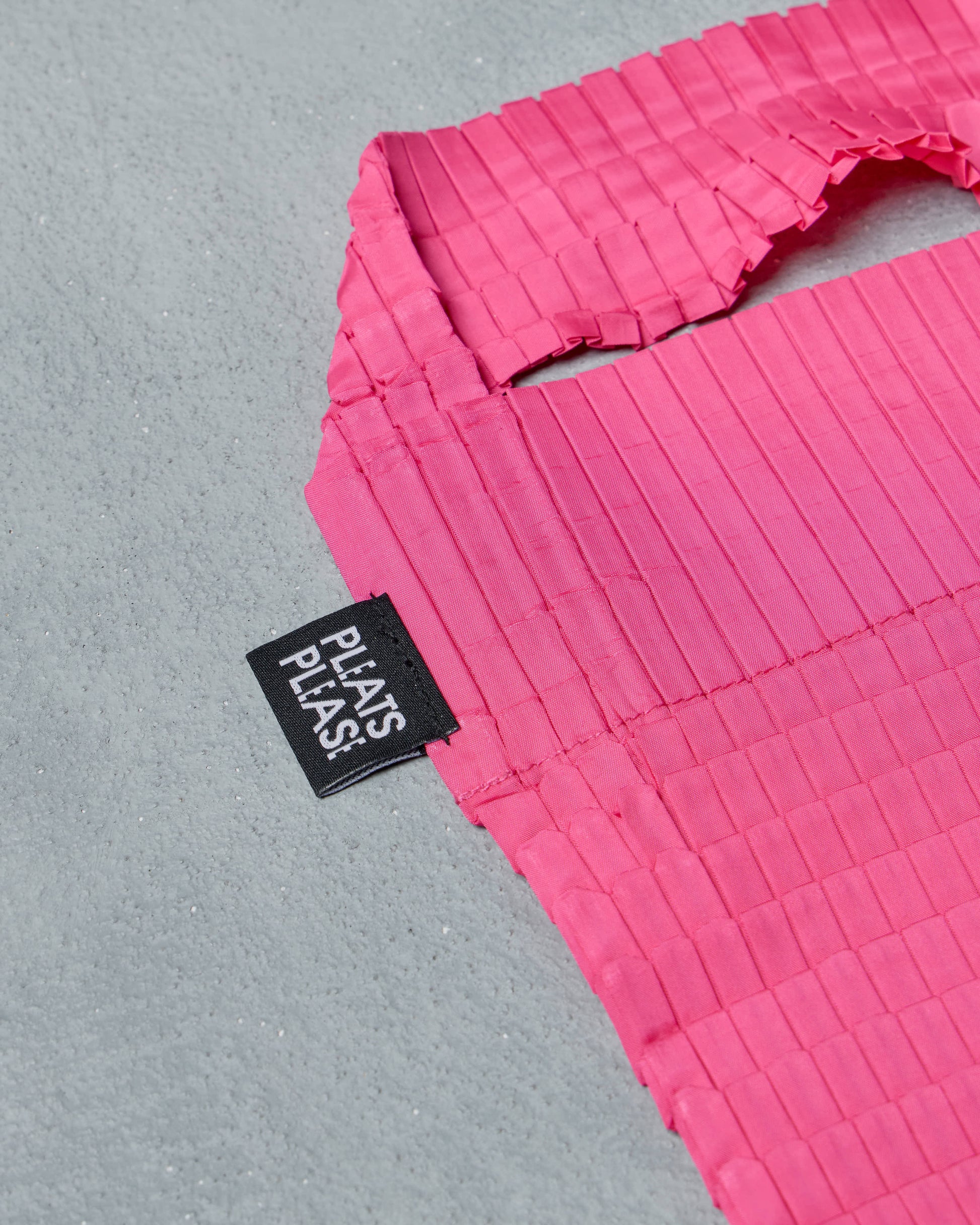 Close-up of a pink textured Issey Miyake Pleats Please bag with a black label on a gray background