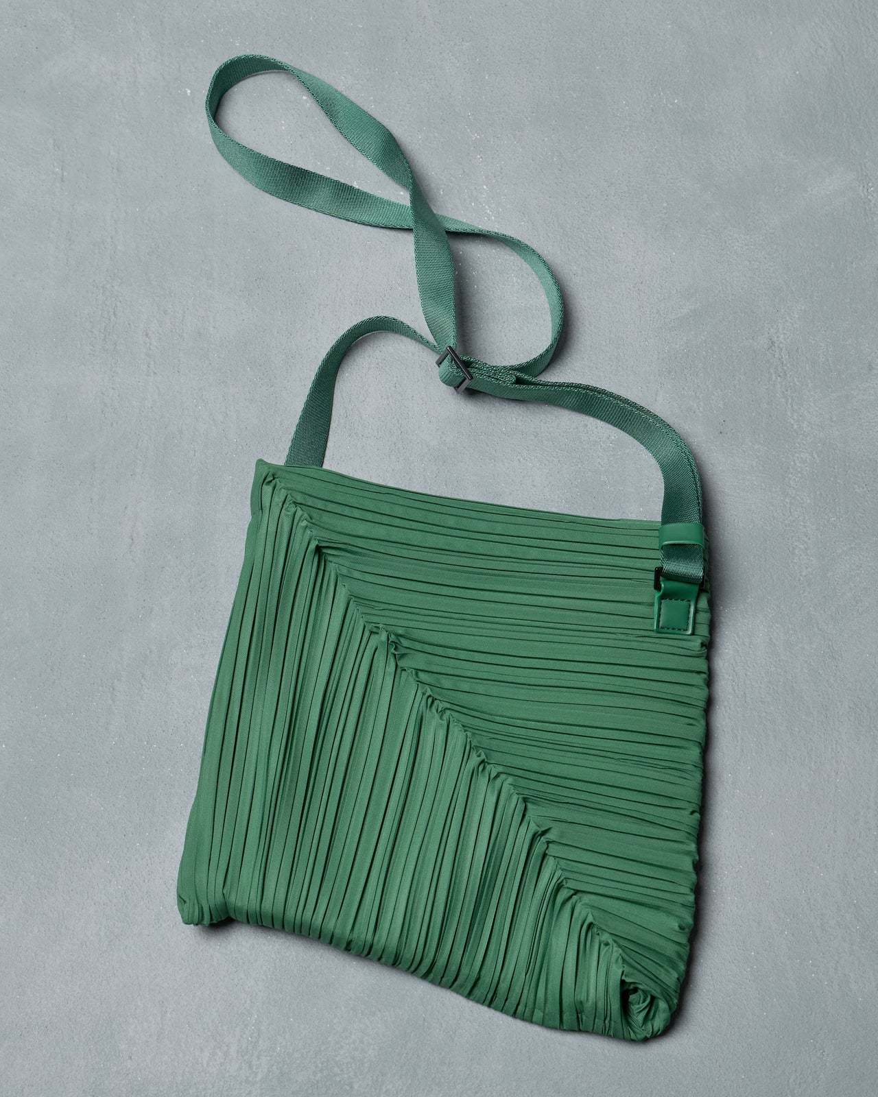 Green pleated Issey Miyake Pleats Please handbag on a light gray background