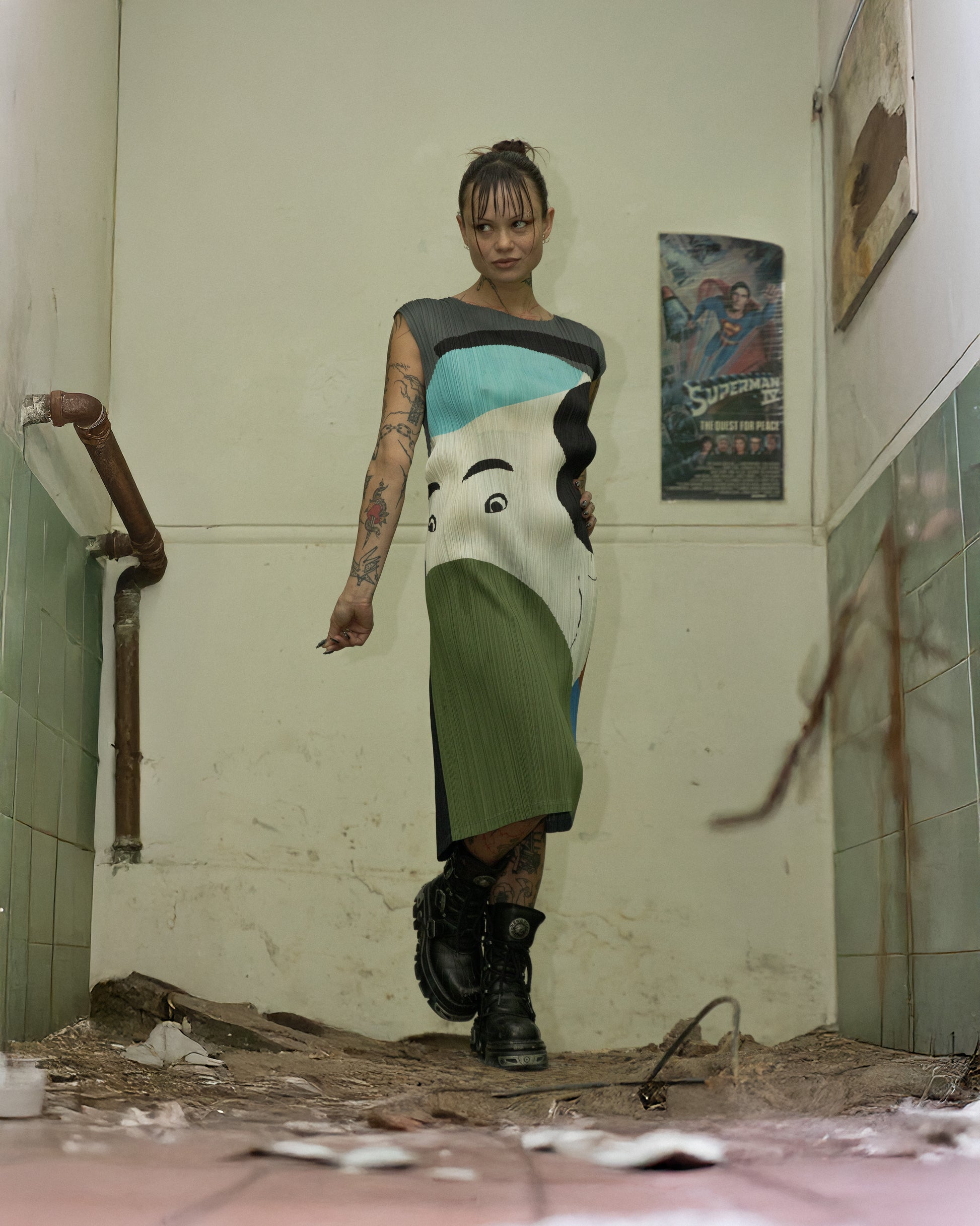 A person standing in a dilapidated room wearing a sleeveless dress with a graphic design by Ikko Tanaka x Issey Miyake.