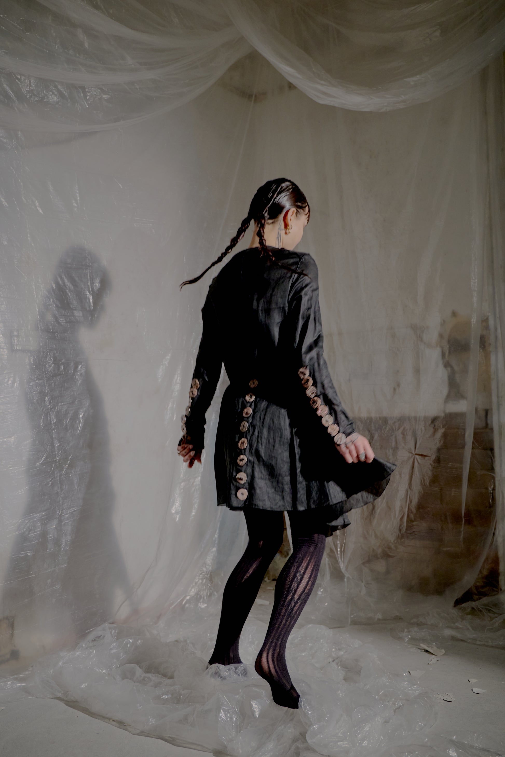 Person wearing a dark Jean Paul Gaultier outfit with decorative buttons in a draped fabric setting