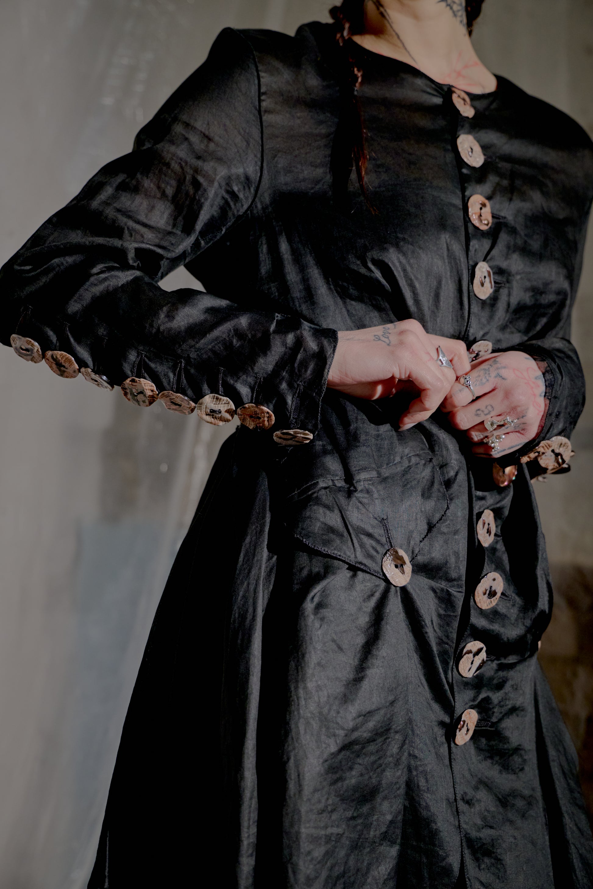 Person wearing a dark Jean Paul Gaultier coat with buttons.