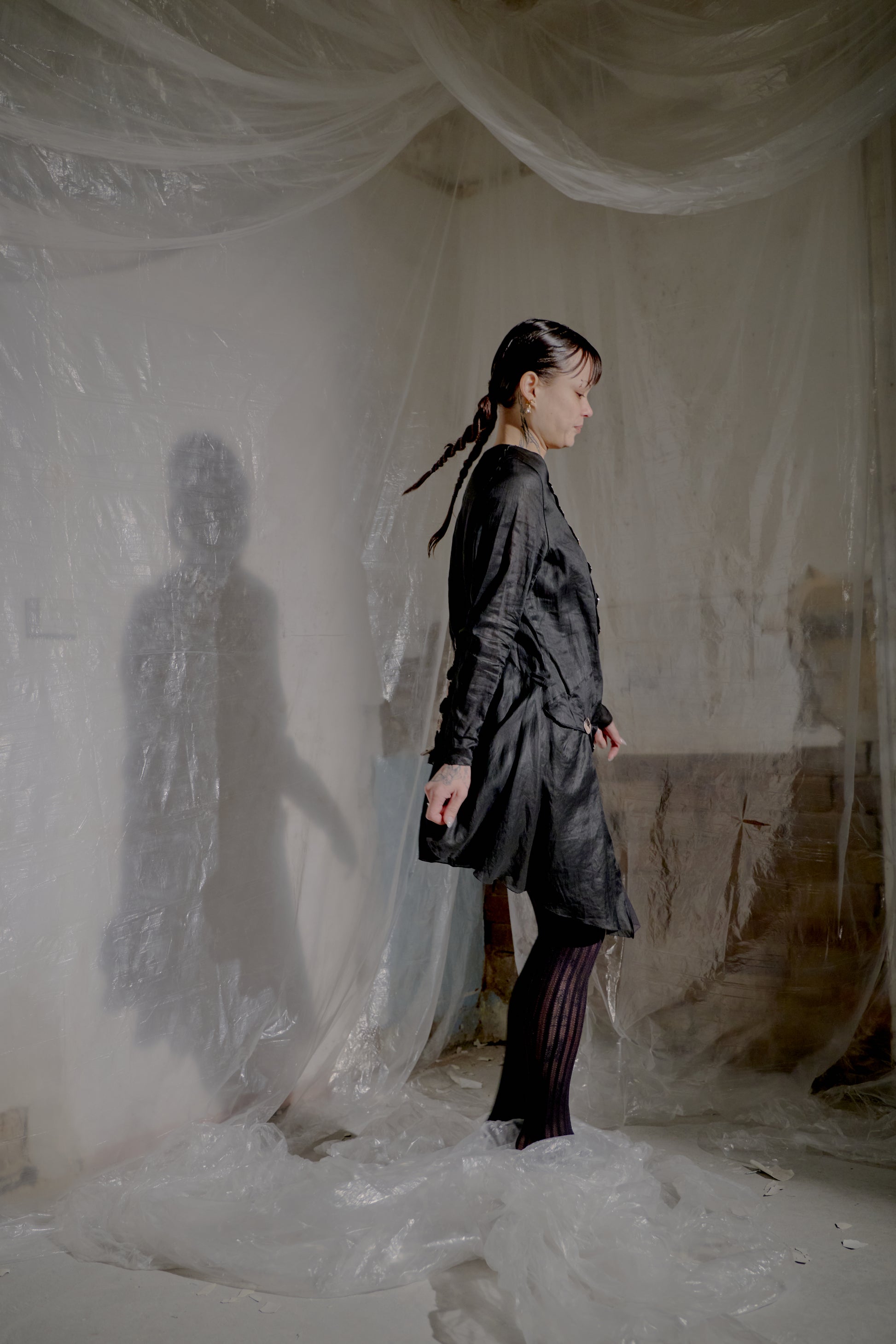 Woman in a black Jean Paul Gaultier outfit standing in a room with white plastic sheeting.