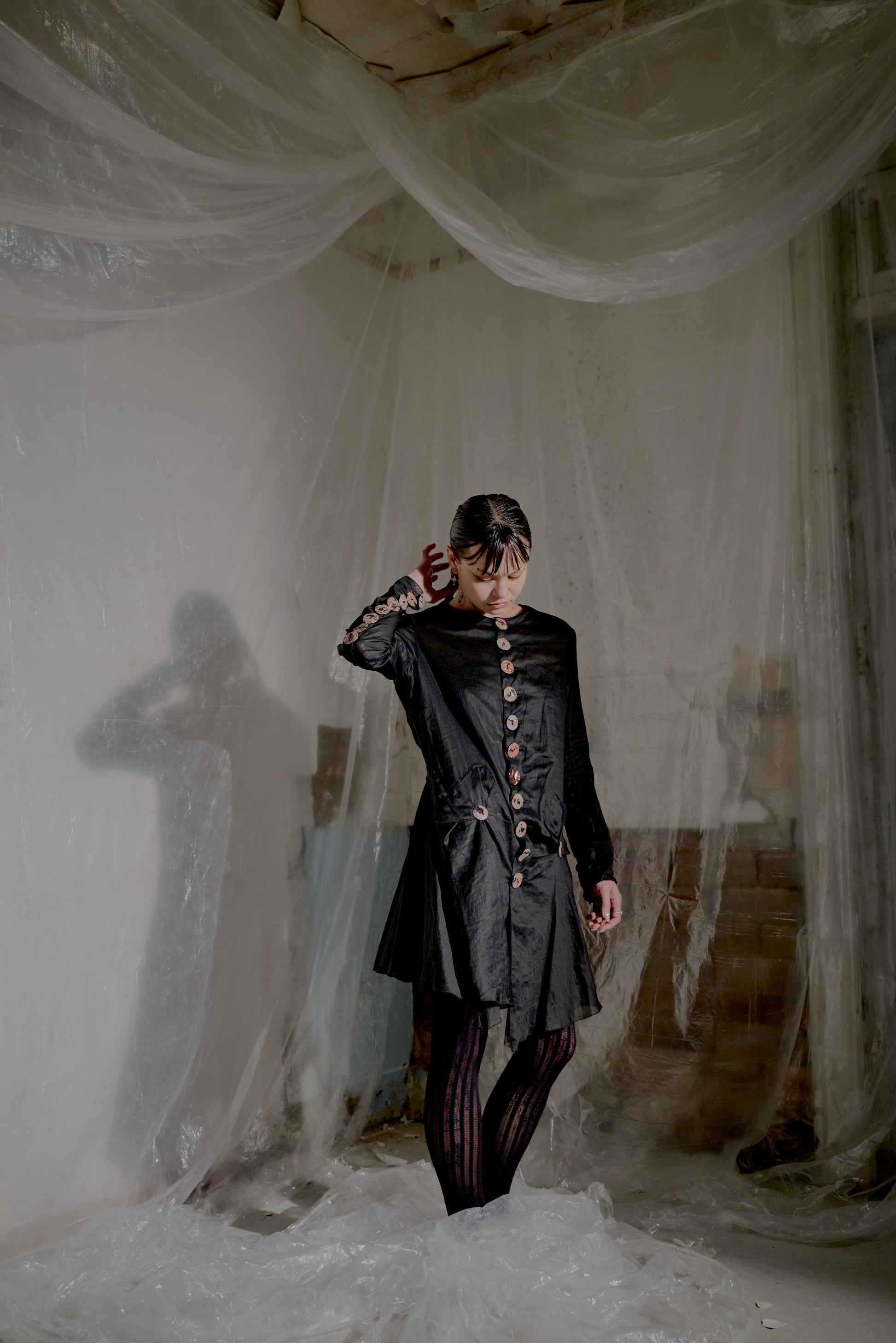 Person in a dark Jean Paul Gaultier jacket standing in a room with draped white fabric
