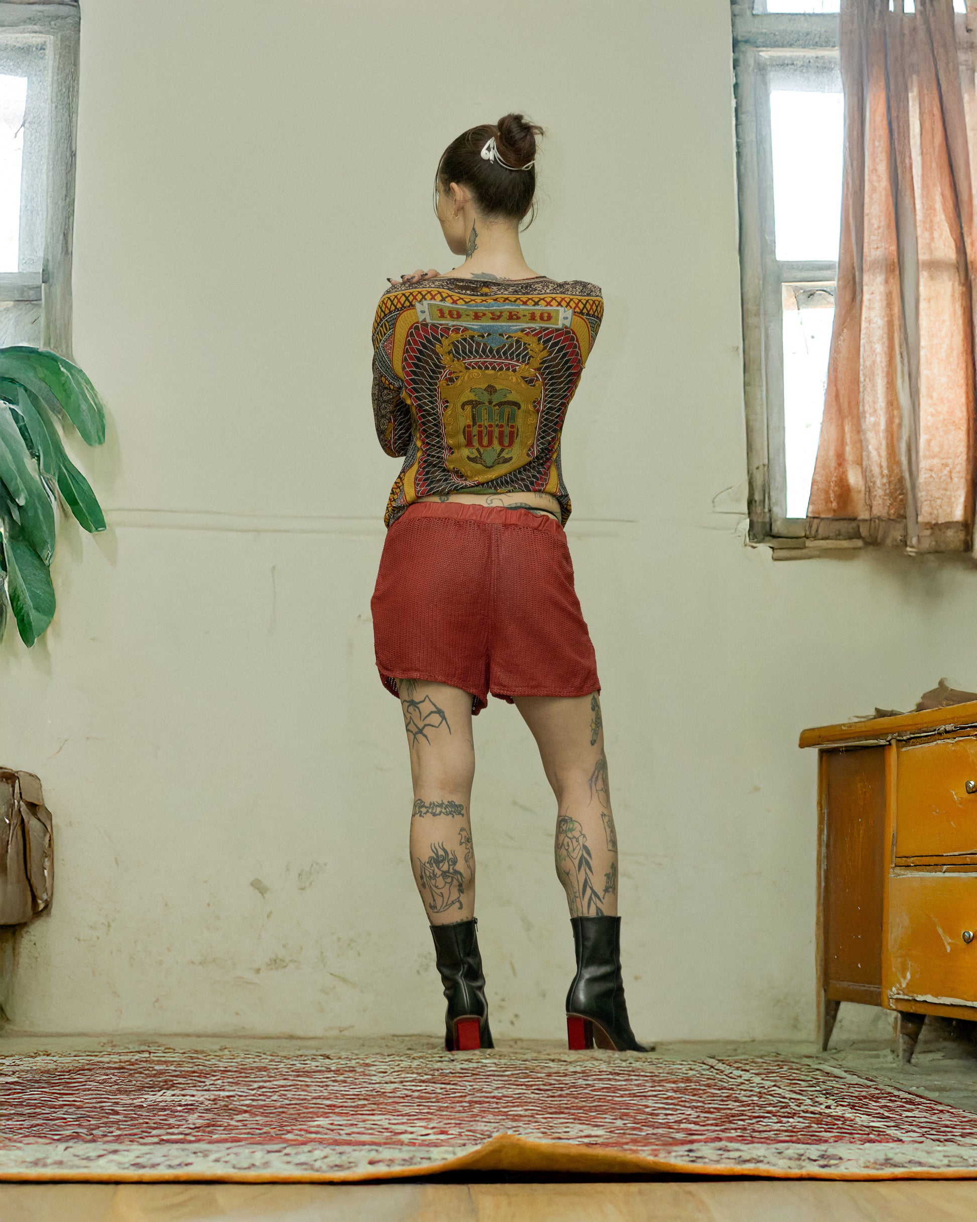 Person wearing a Jean Paul Gaultier patterned top and red shorts standing in a room with a window and furniture.