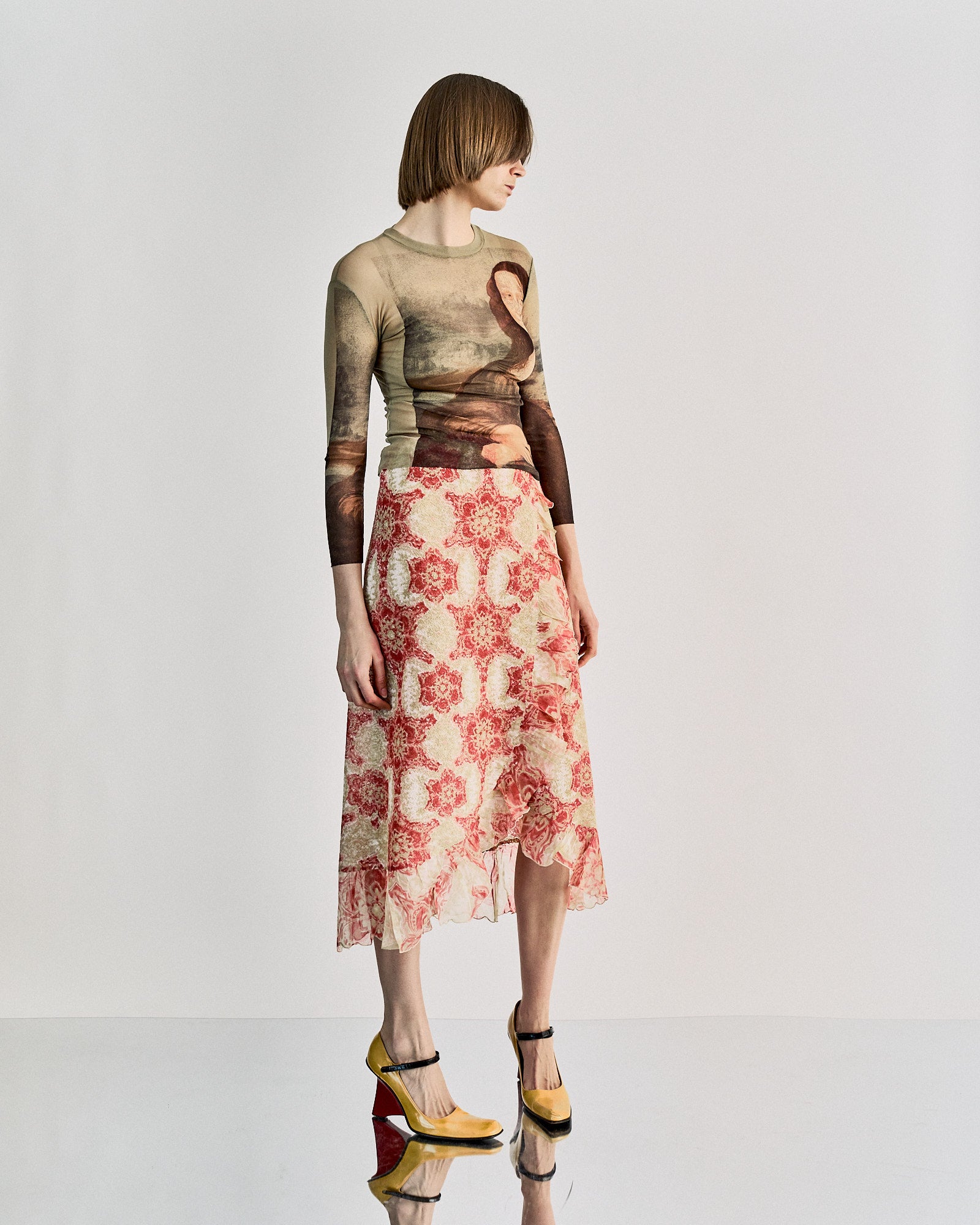 A model wearing a Jean Paul Gaultier SS 1995 Mona Lisa mesh top, with an all-over print of Leonardo DaVinci's Mona Lisa, in a showcasing setting.