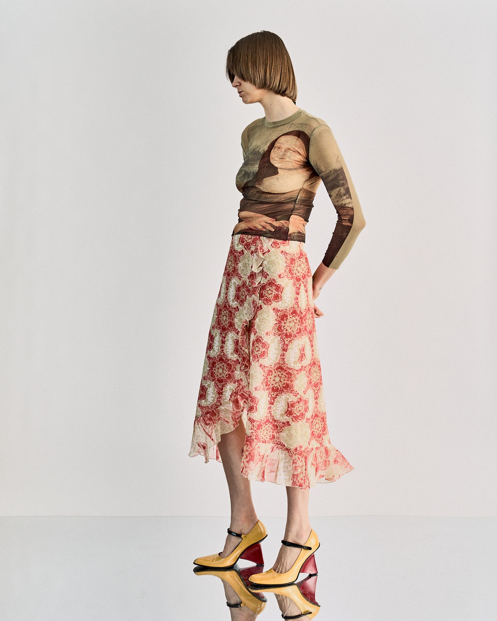 A person wears a sheer, tight-fitting Jean Paul Gaultier top featuring the Mona Lisa print, paired with a skirt with red and white floral patterns, exuding an artistic vibe.