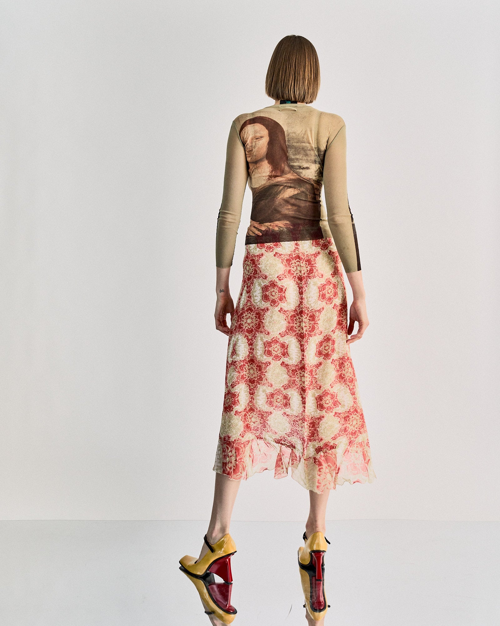 A model wearing a Jean Paul Gaultier SS 1995 Mona Lisa mesh top, with an all-over print of Leonardo DaVinci's Mona Lisa, in a showcasing setting.