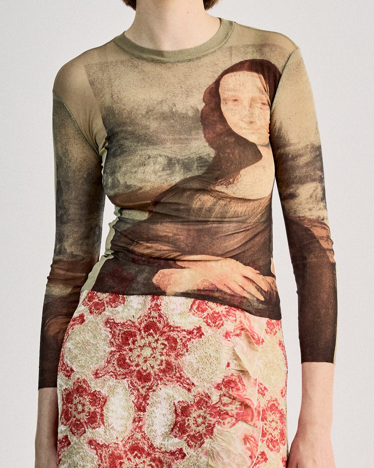 A model wearing a Jean Paul Gaultier SS 1995 Mona Lisa mesh top, with an all-over print of Leonardo DaVinci's Mona Lisa, in a showcasing setting.