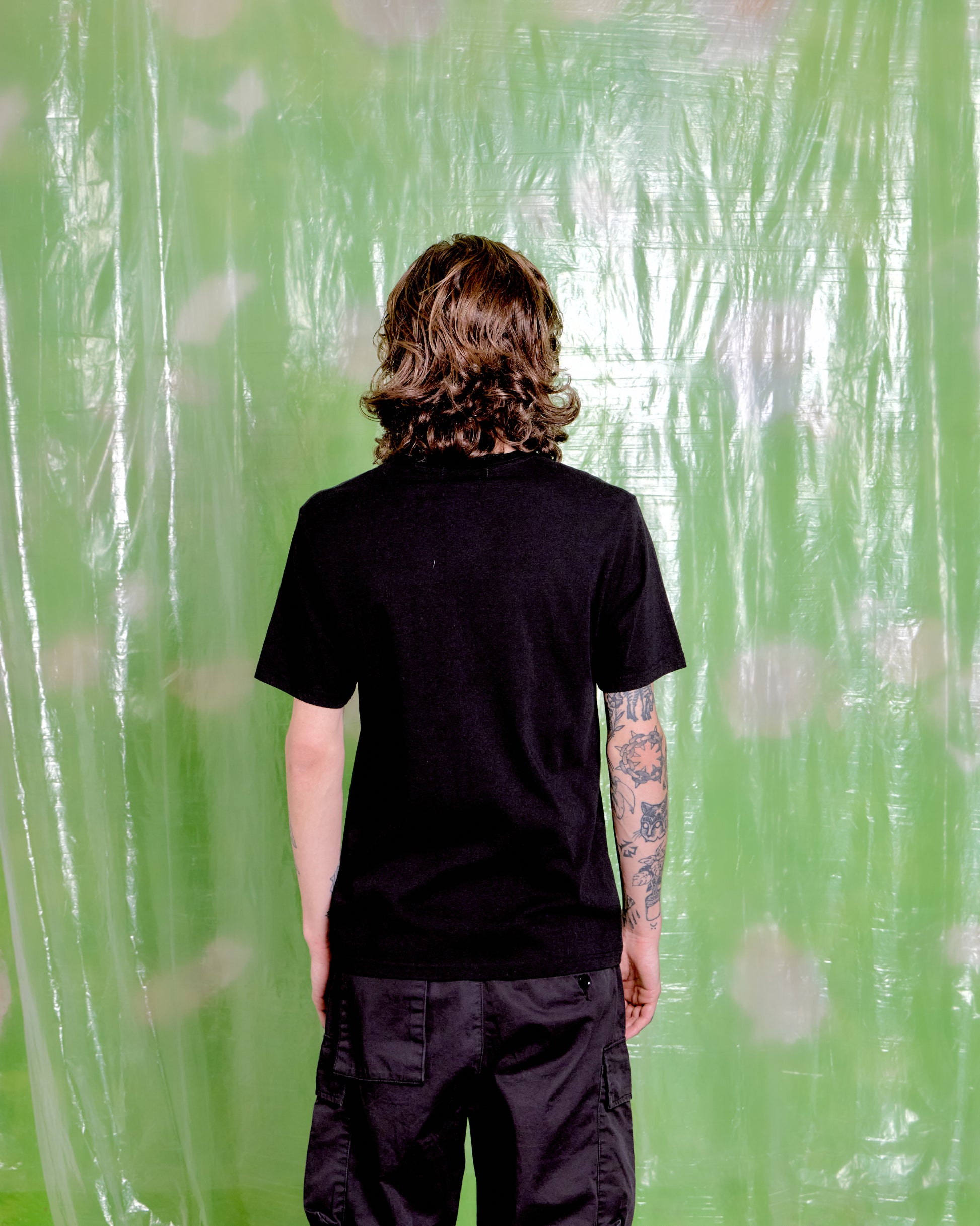 Person wearing a black t-shirt and pants standing in front of a green patterned curtain