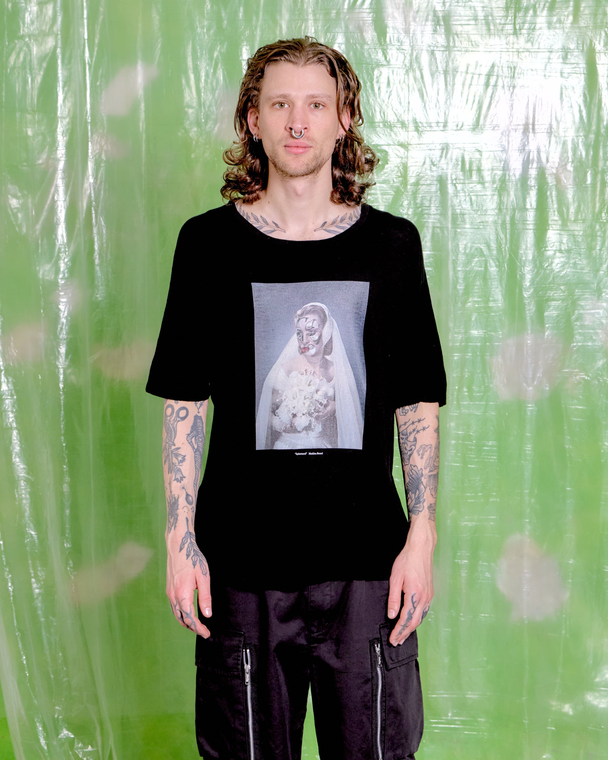 Person wearing a black t-shirt with a graphic design against a green patterned background