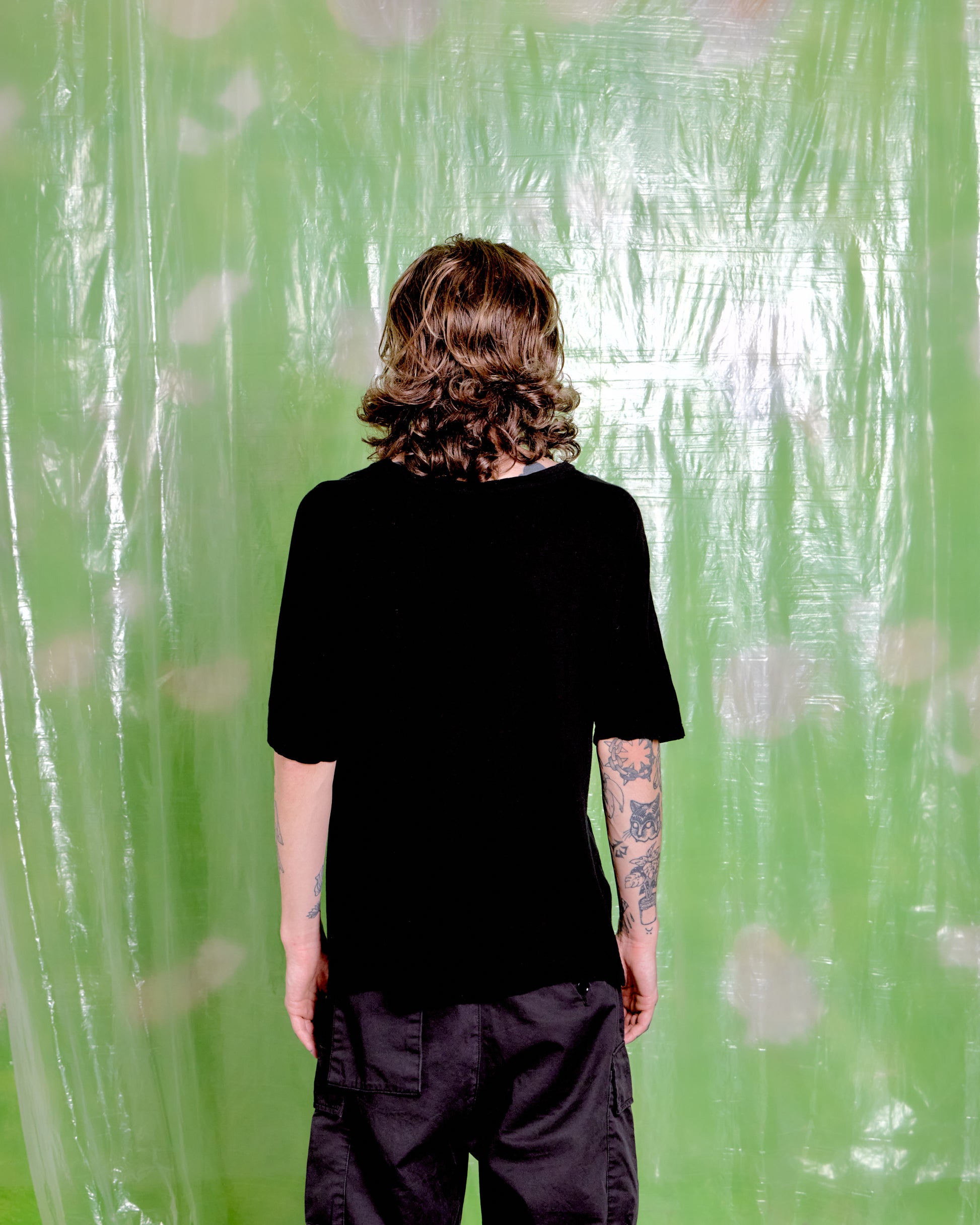 Person wearing a black t-shirt and pants standing in front of a green patterned curtain