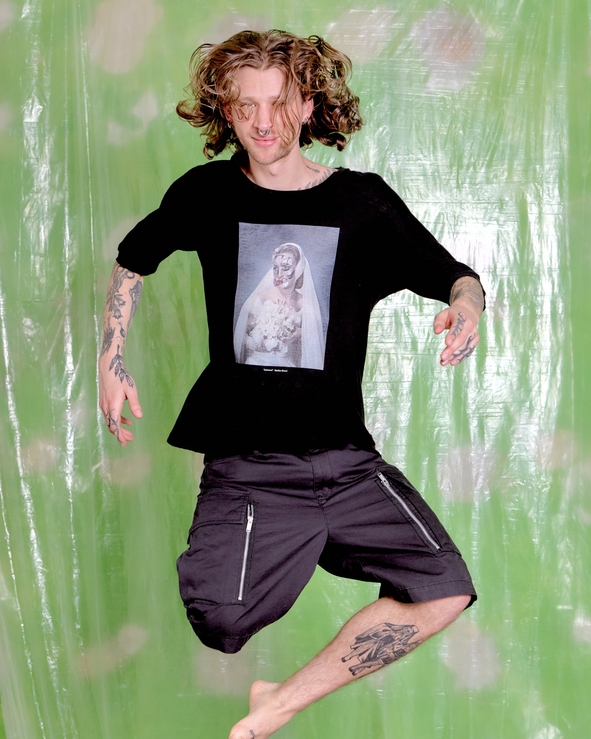 Person wearing a black t-shirt with a graphic design and black shorts against a green textured background