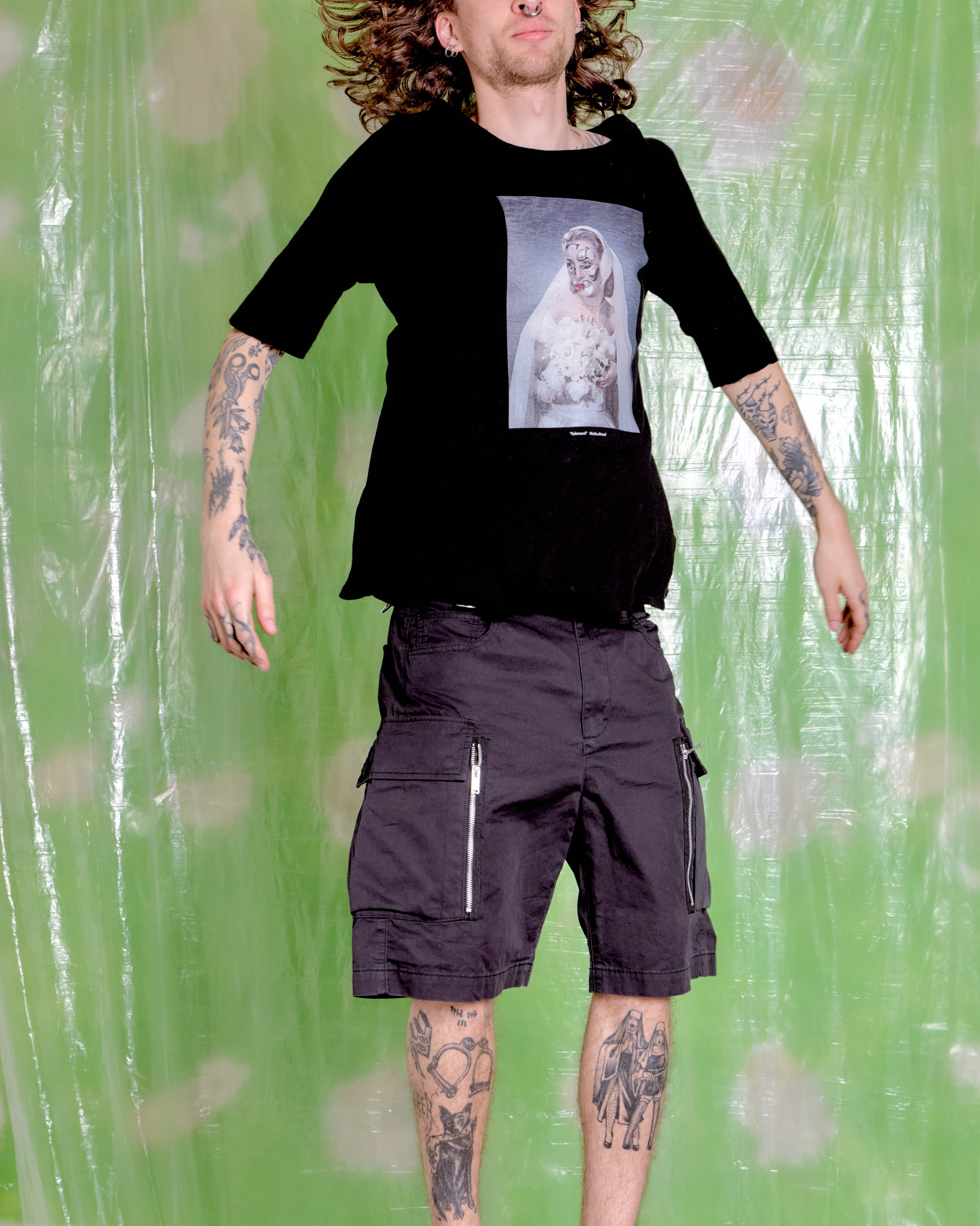 Person wearing a black t-shirt with a graphic design and black cargo shorts against a green background