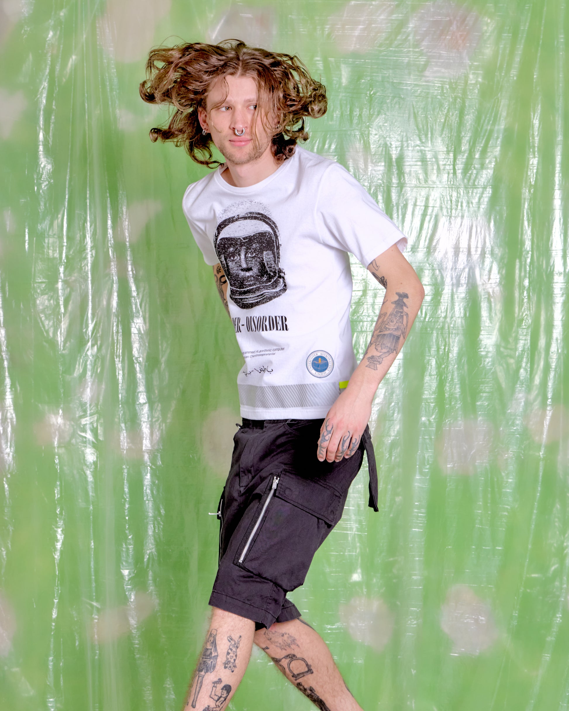 Person wearing a white t-shirt with a graphic design and black shorts against a green background
