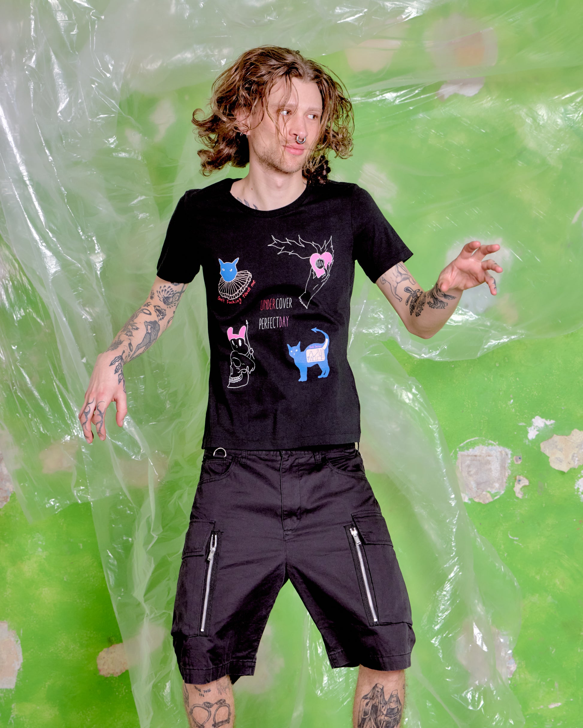 Person wearing a black t-shirt with graphic designs against a green and clear plastic background
