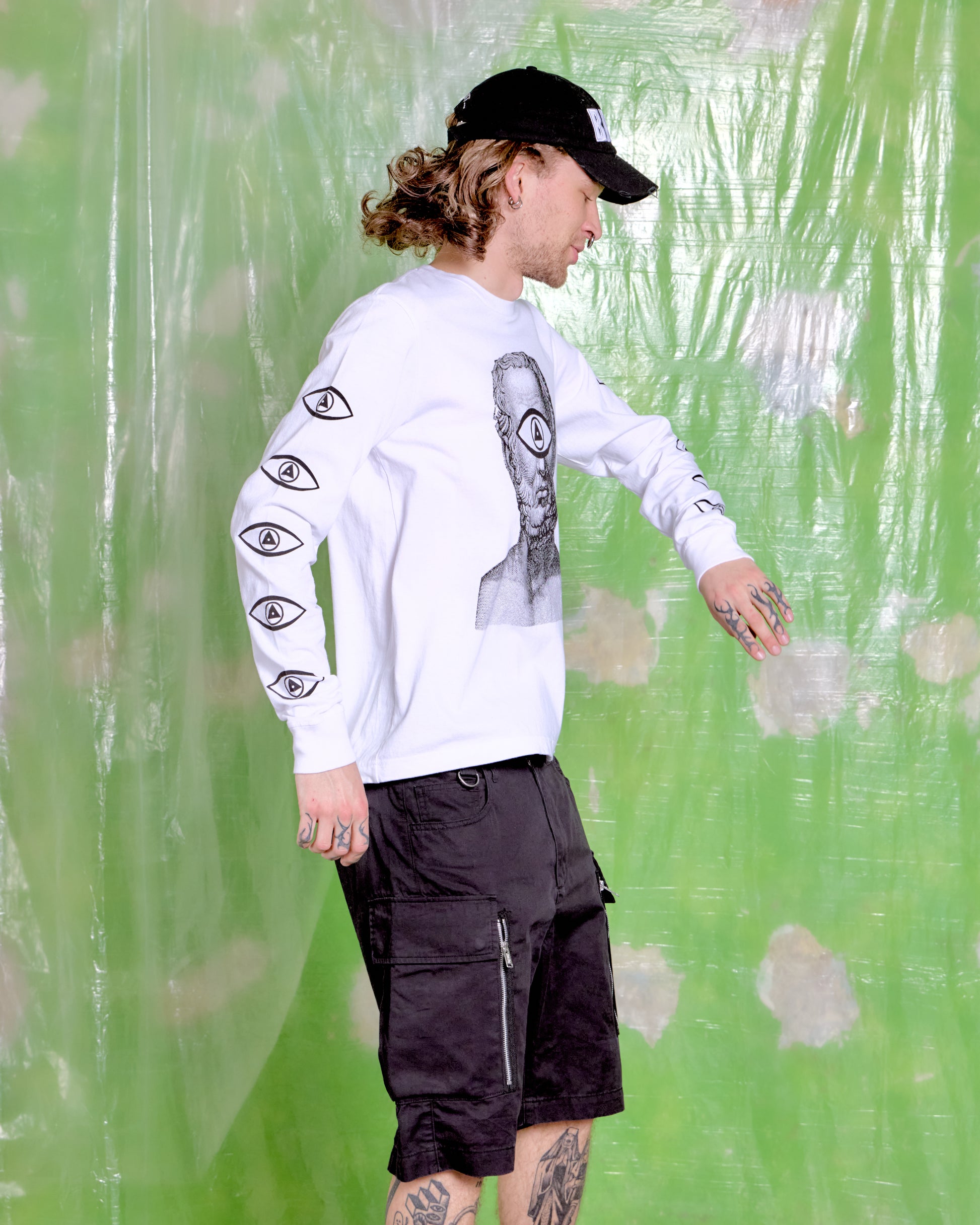 Person wearing a white long-sleeve shirt with black designs and black shorts against a green patterned background