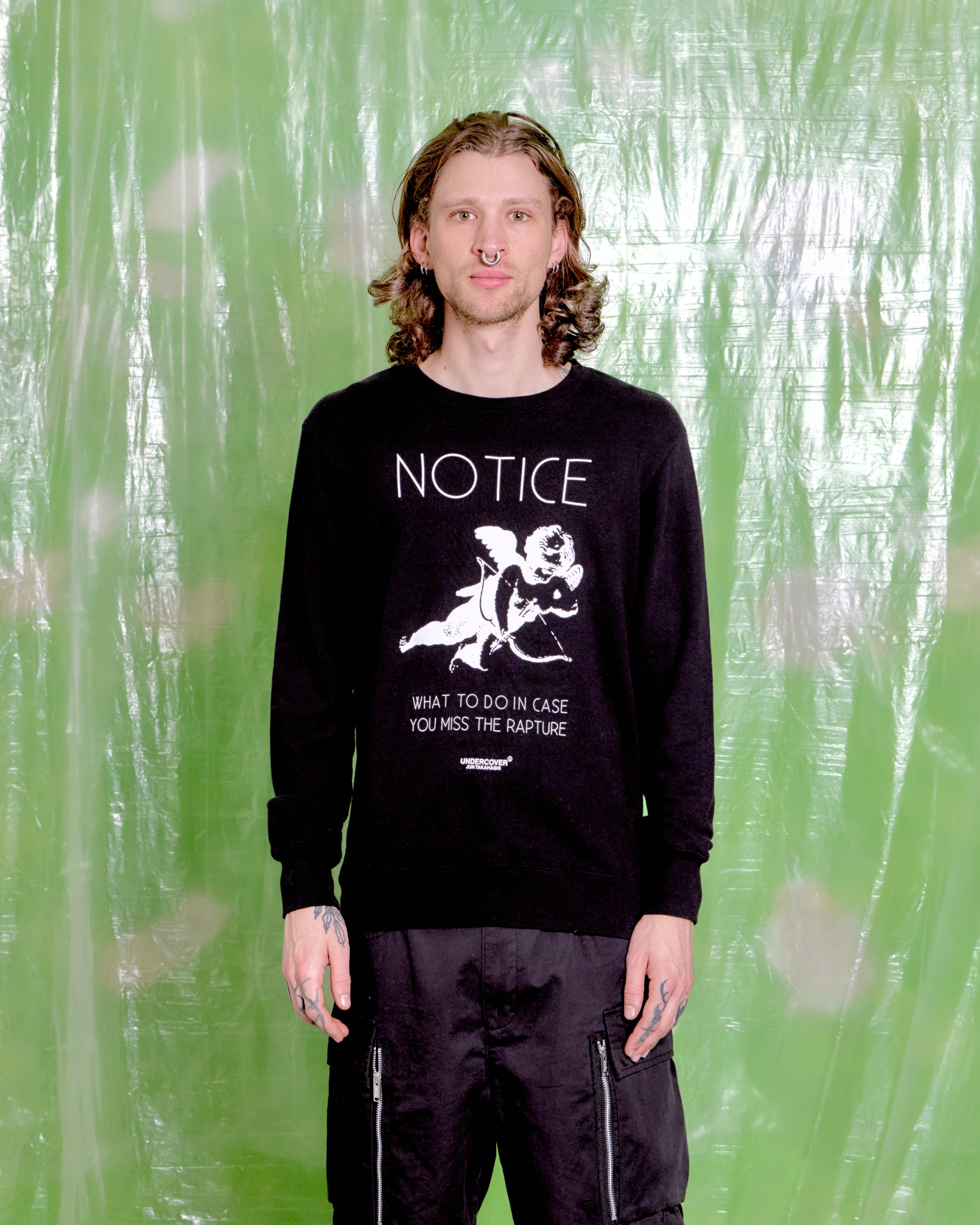Person wearing a black sweatshirt with white text and graphics against a green textured background