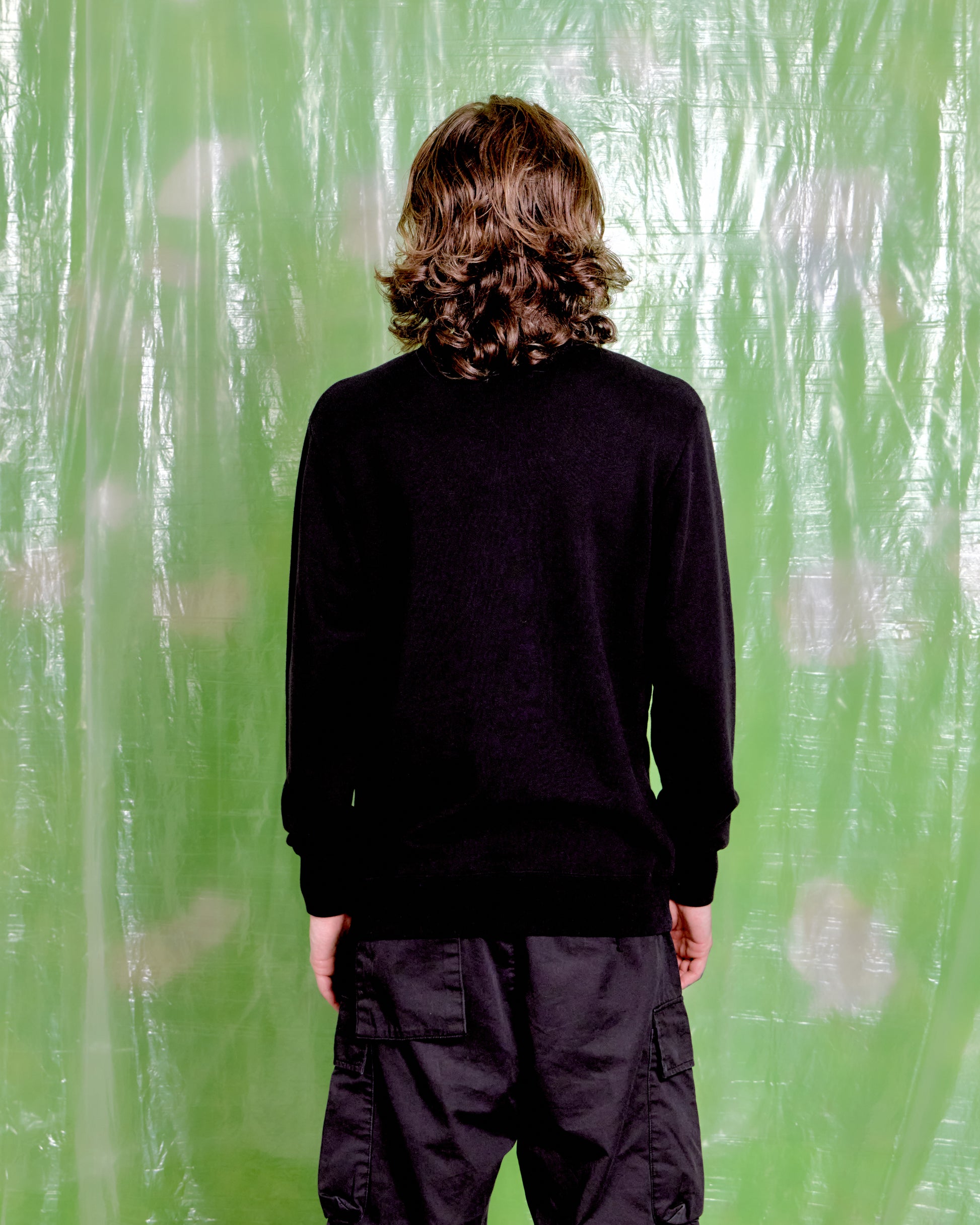 Person wearing a black sweater and pants standing in front of a green textured wall.