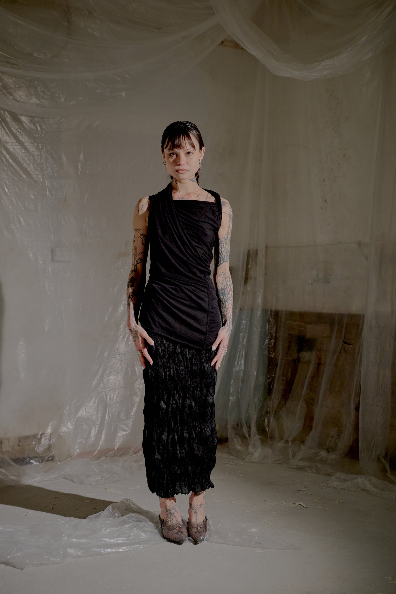 Person wearing a black sleeveless top and pants in a room with white draped fabric.