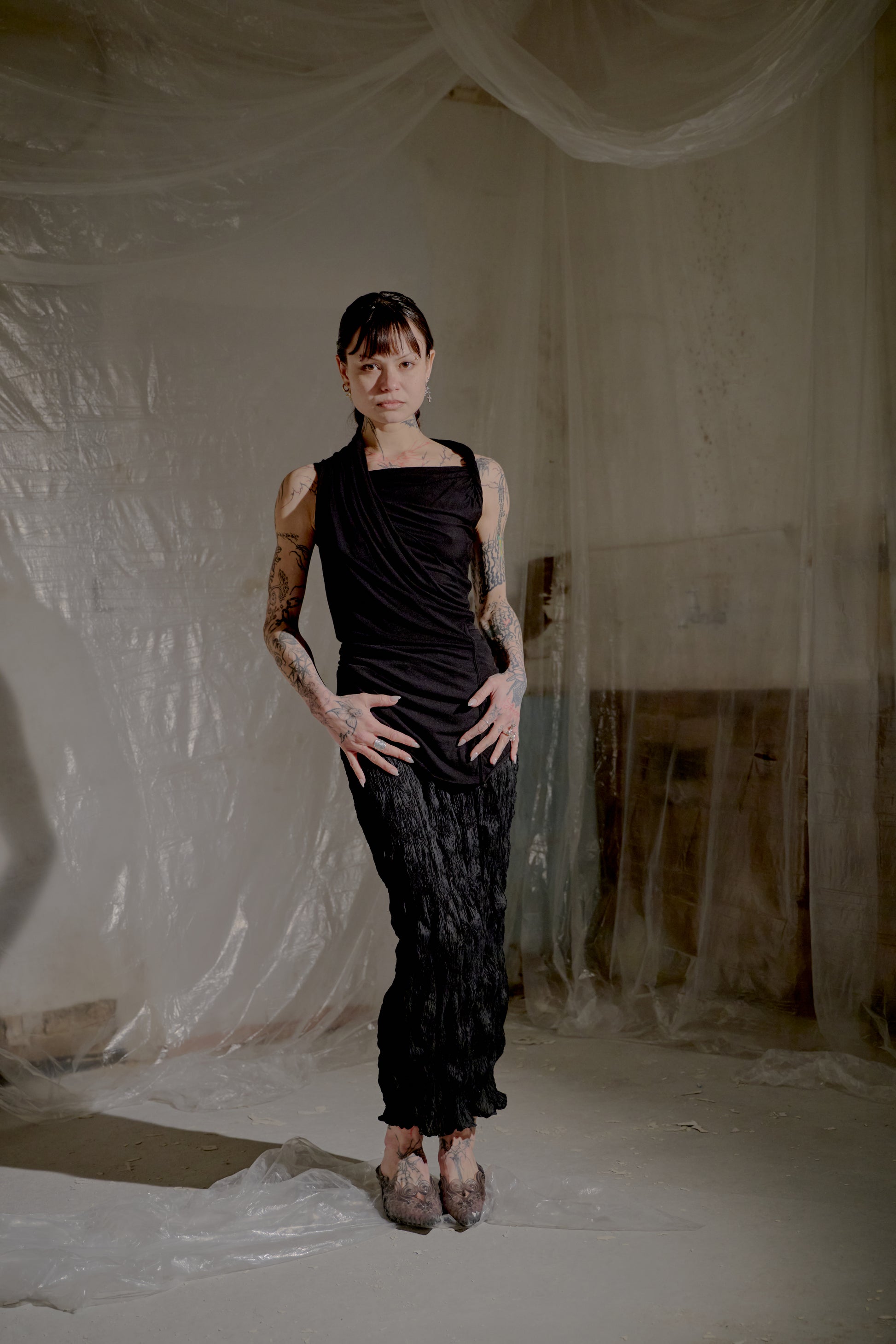 Person wearing a black sleeveless top and pants in a room with white draped fabric.