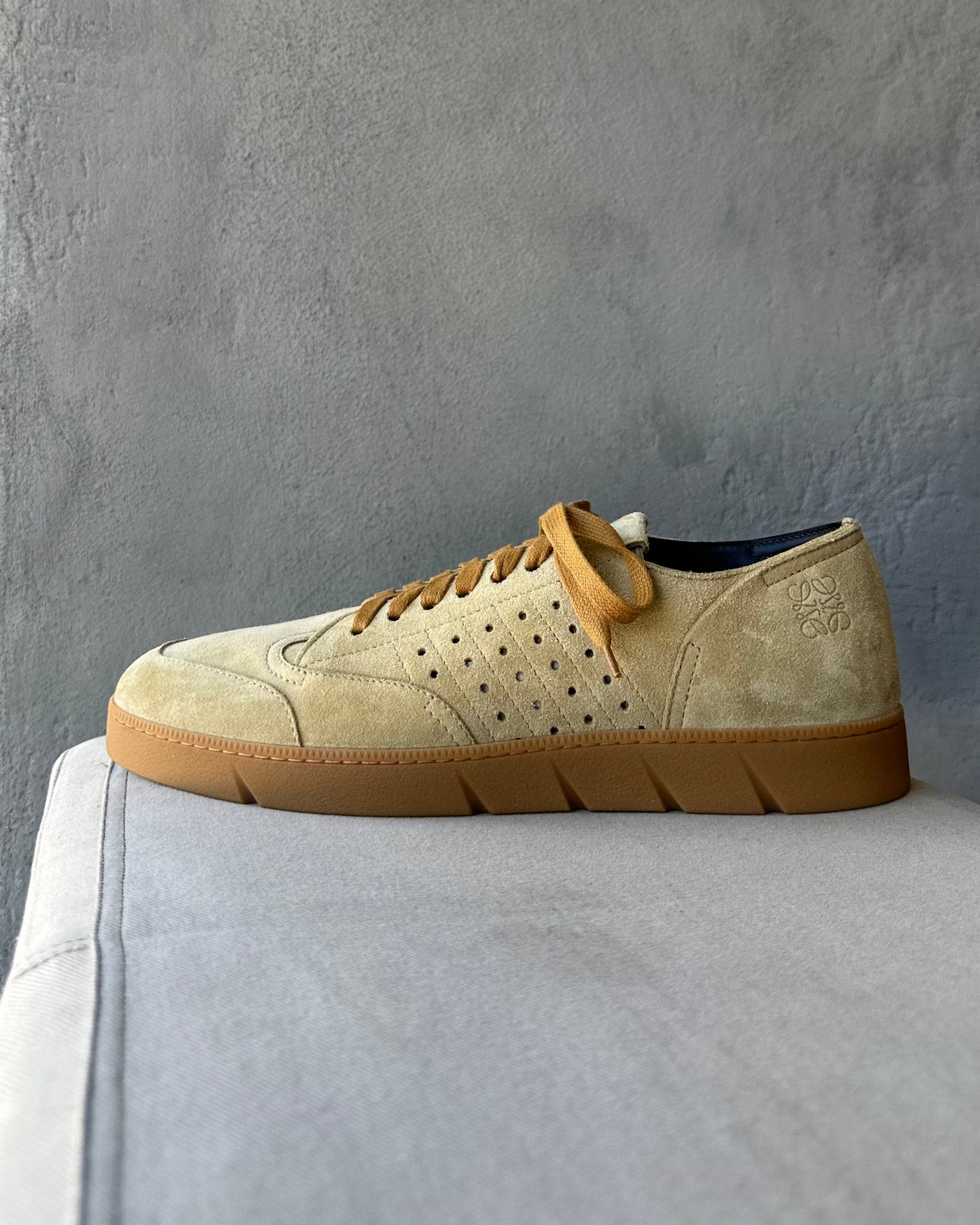 Beige Loewe sneaker with brown sole on a gray surface against a gray background
