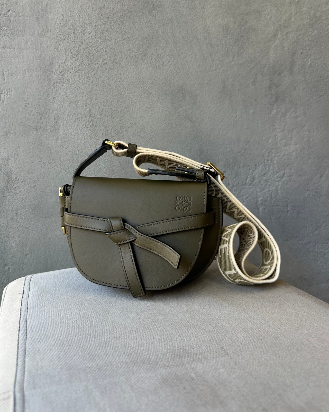 Green leather Loewe handbag with a strap on a gray surface against a gray background