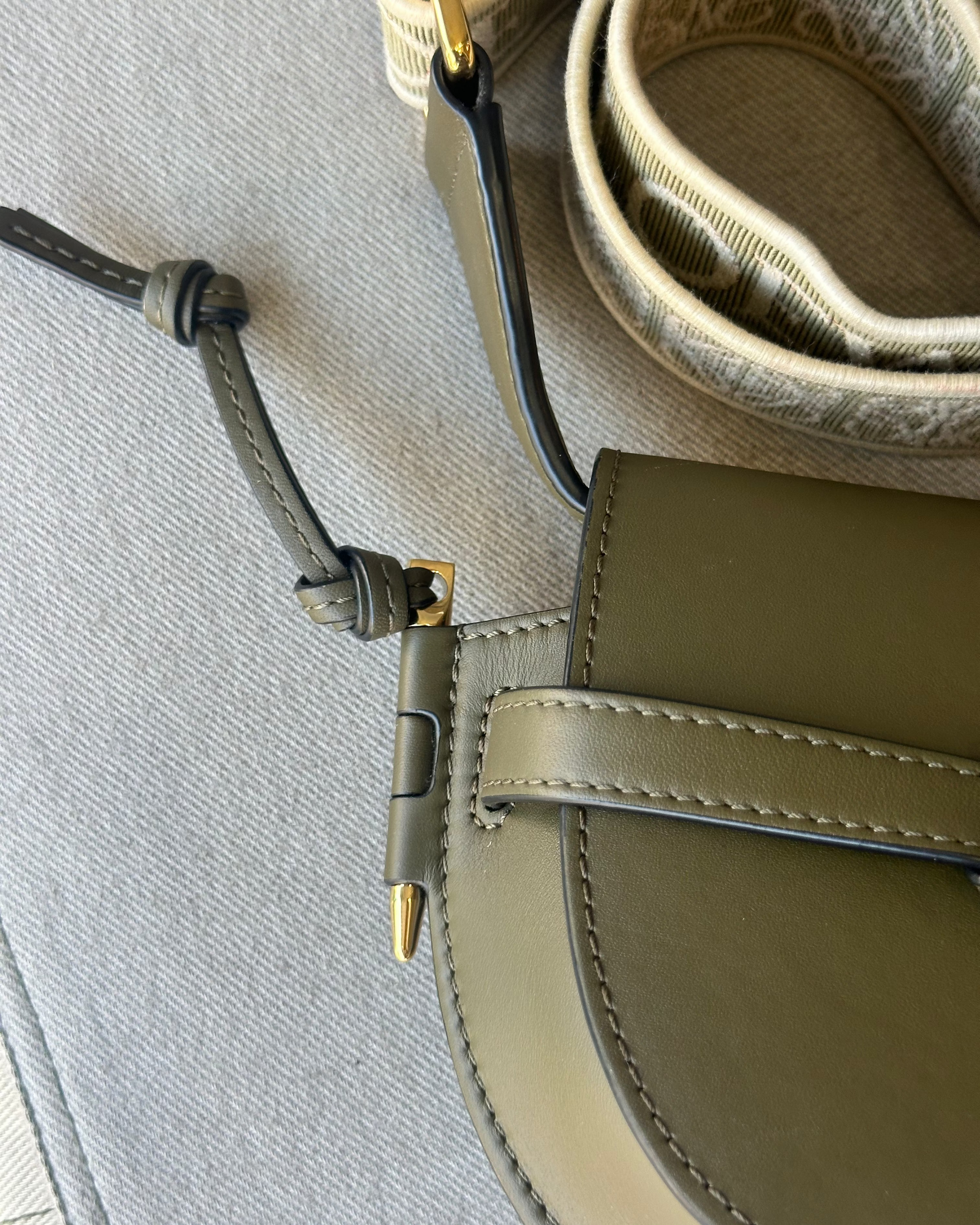 Close-up of a green leather Loewe handbag with a strap on a gray surface