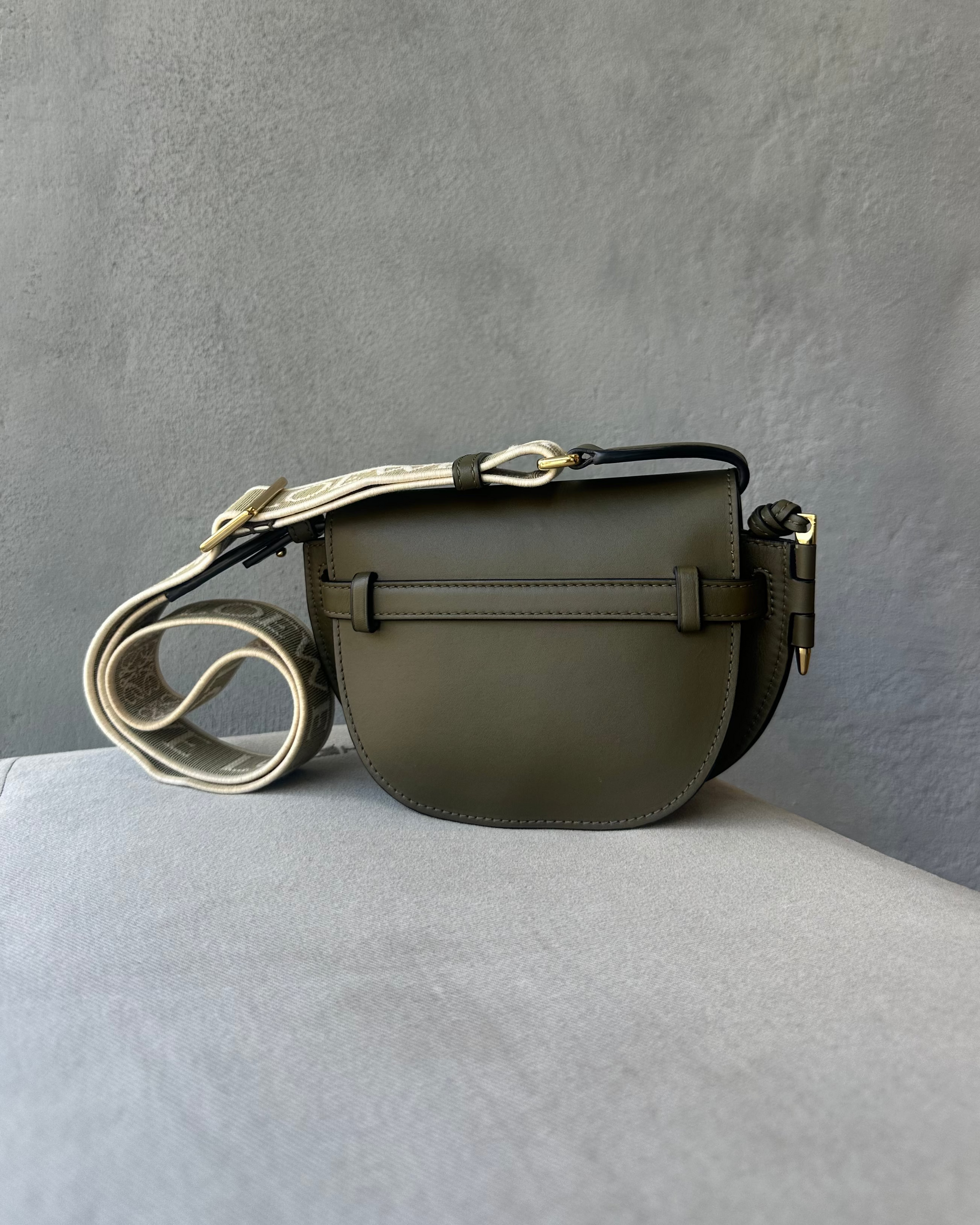 Green leather Loewe crossbody bag on a gray surface with a gray background
