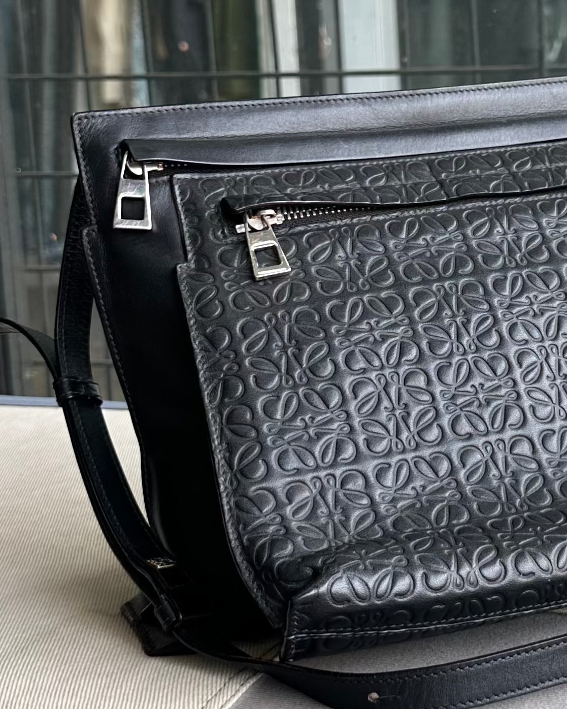 Black embossed Loewe leather bag with a zipper on a light surface.