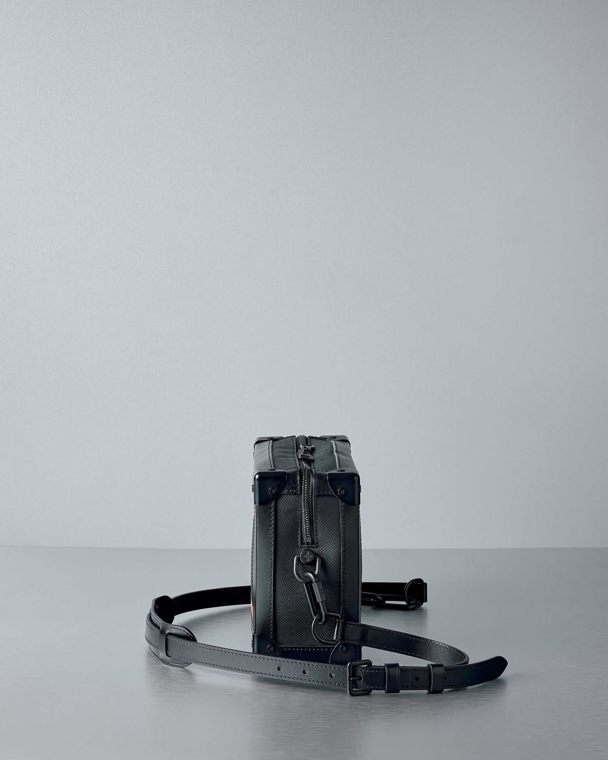 Black leather Louis Vuitton bag with a strap on a light gray background