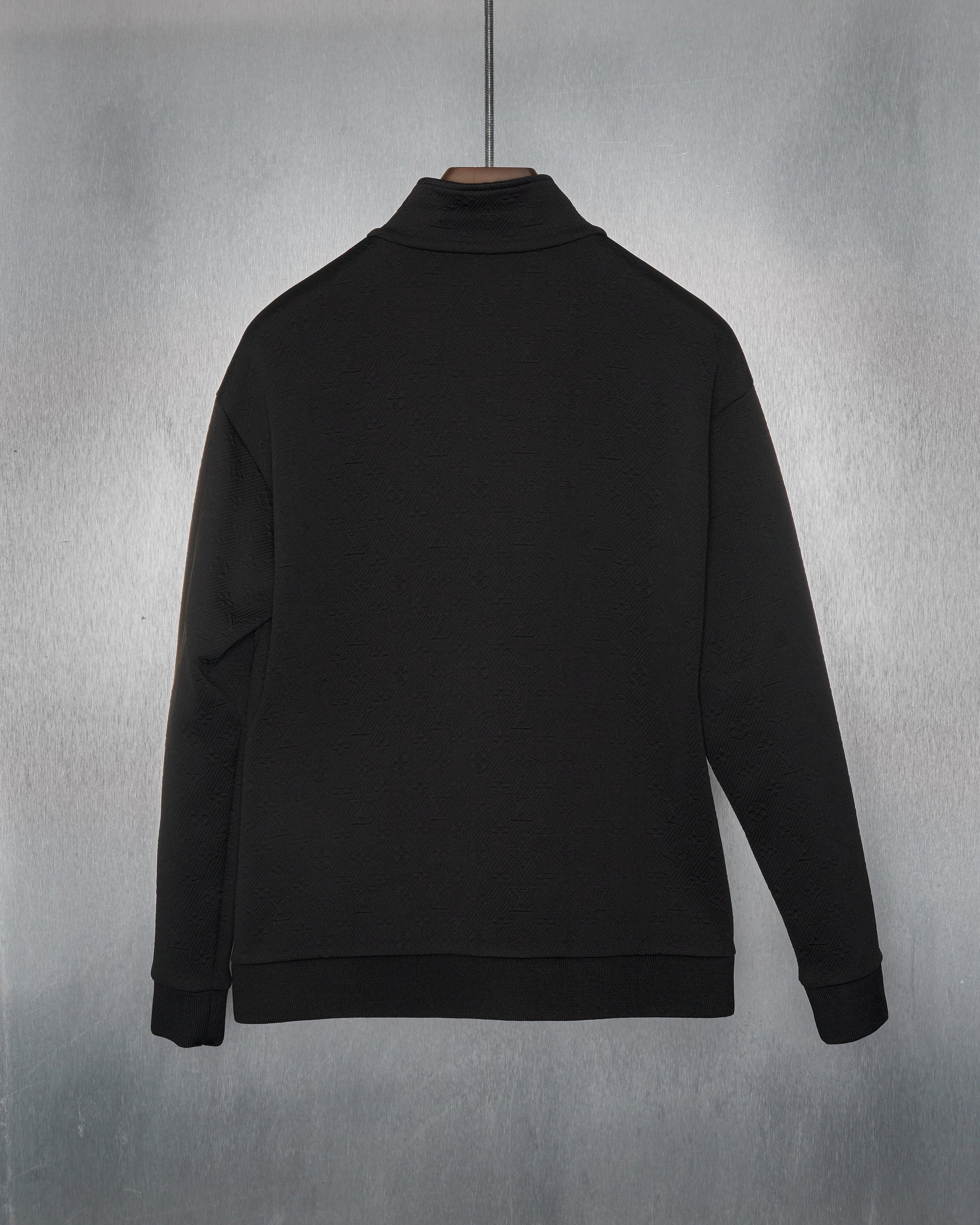 Black Louis Vuitton jacket hanging on a metal hanger against a textured gray background. The jacket is simple, with a ribbed hem and cuffs, exuding a minimalist style.