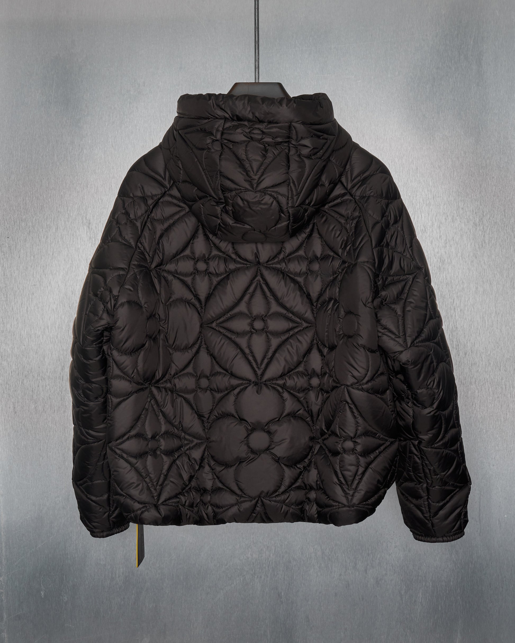 Reverse of a  black Louis Vuitton quilted hoodie jacket with LVSE flower quilting, featuring a hood, zippered closures, and padded cuffs.