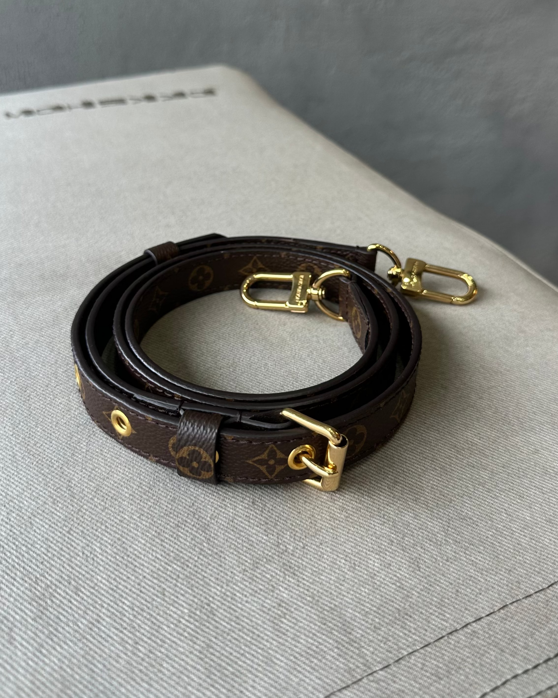 Brown leather Louis Vuitton bag strap with gold hardware on a gray surface