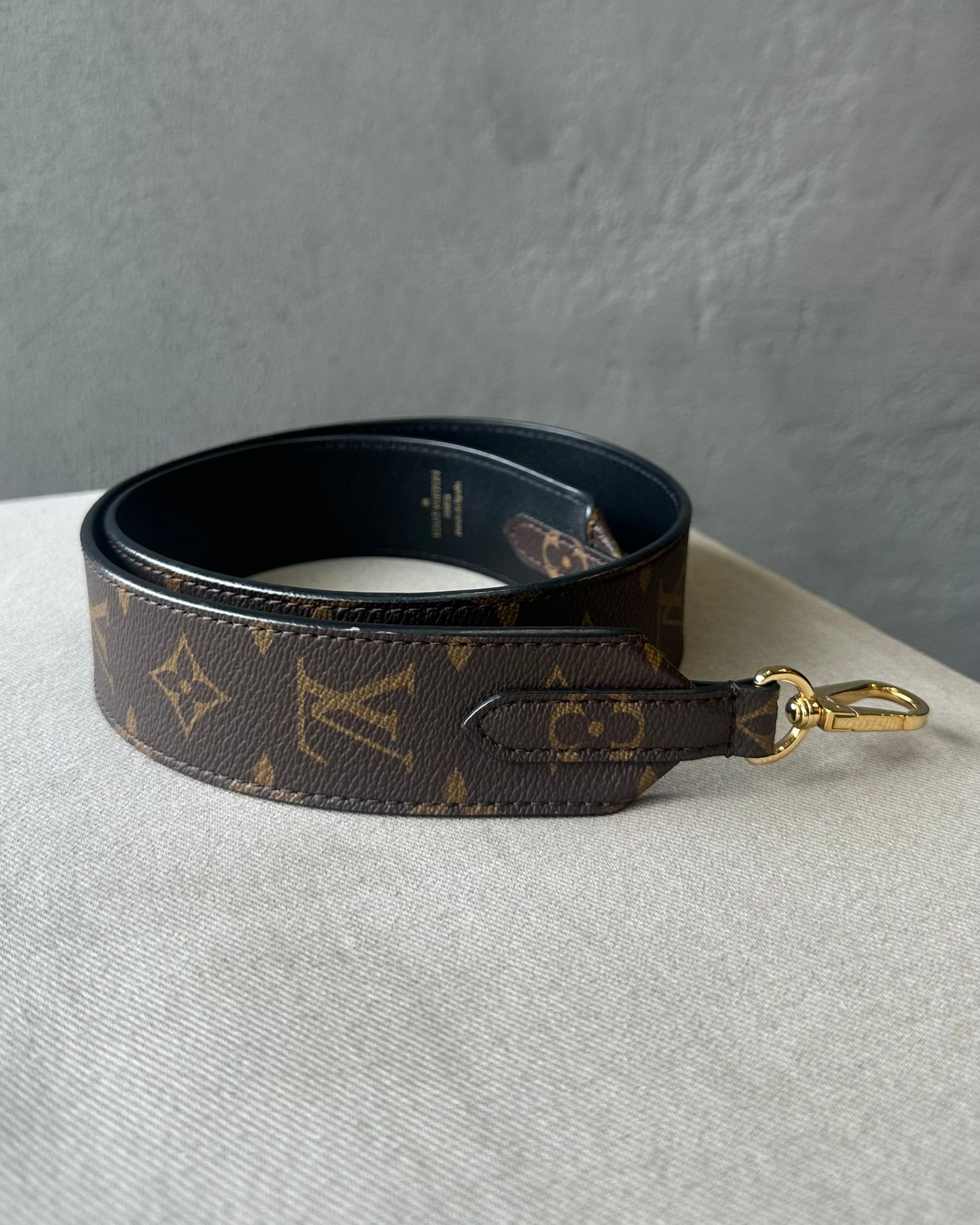 Louis Vuitton monogram bag strap on a light gray surface with a dark gray background