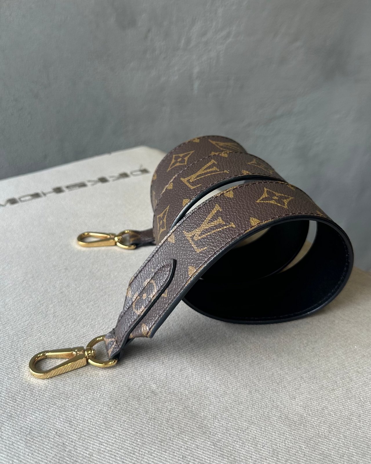 Louis Vuitton monogram bag strap on a light gray surface with a dark gray background