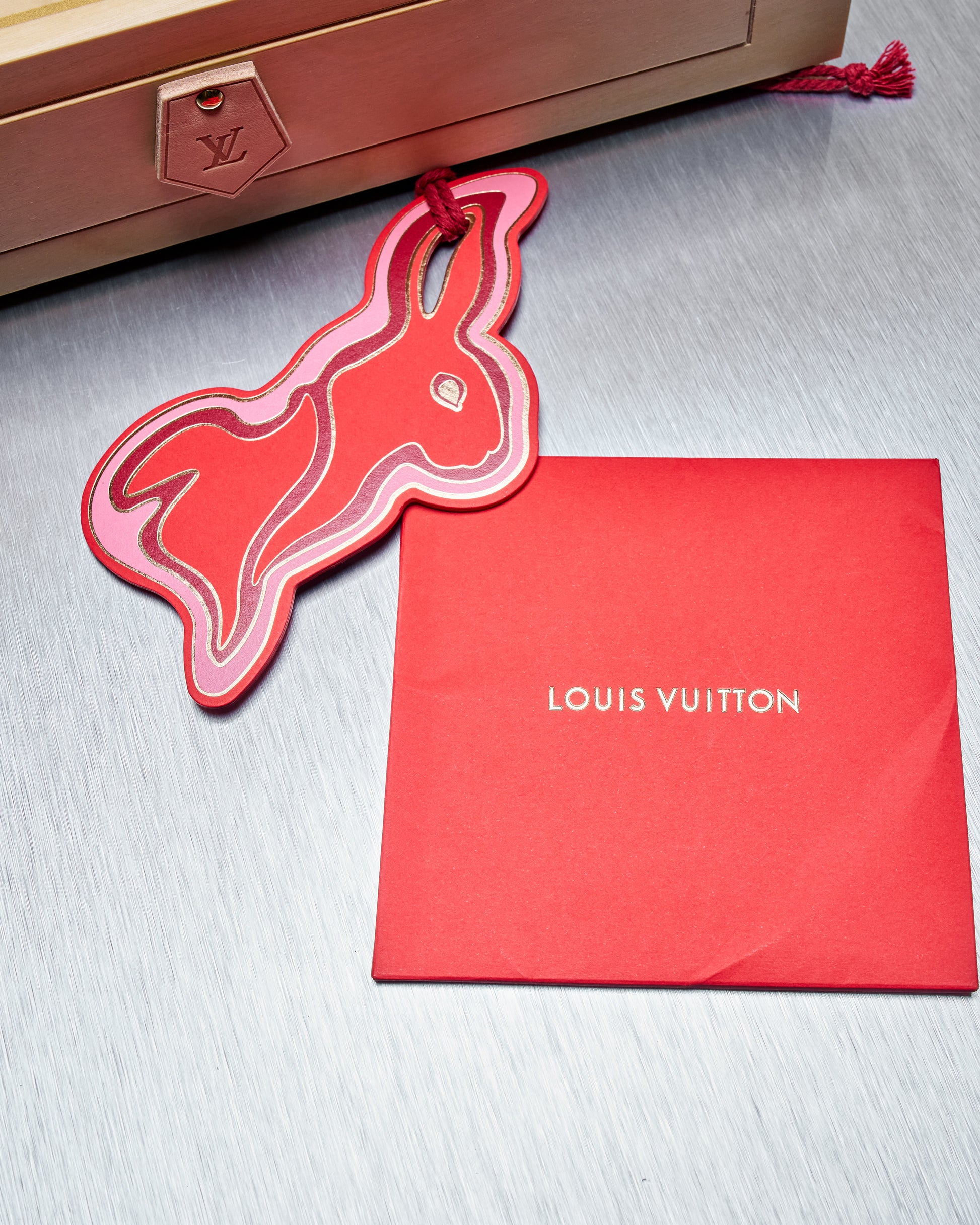 Red 'Louis Vuitton' packaging with a matching rabbit-shaped tag on a gray surface.