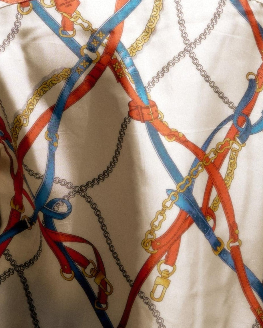Patterned Louis Vuitton fabric featuring intertwined red and blue straps with gold chains and buckles on a beige background, creating an elegant, dynamic design.