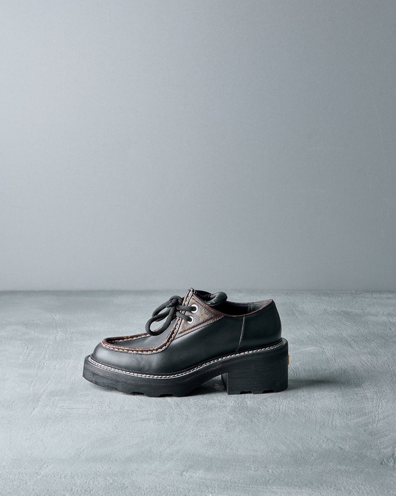 Black leather Louis Vuitton shoe with brown accents on a gray background