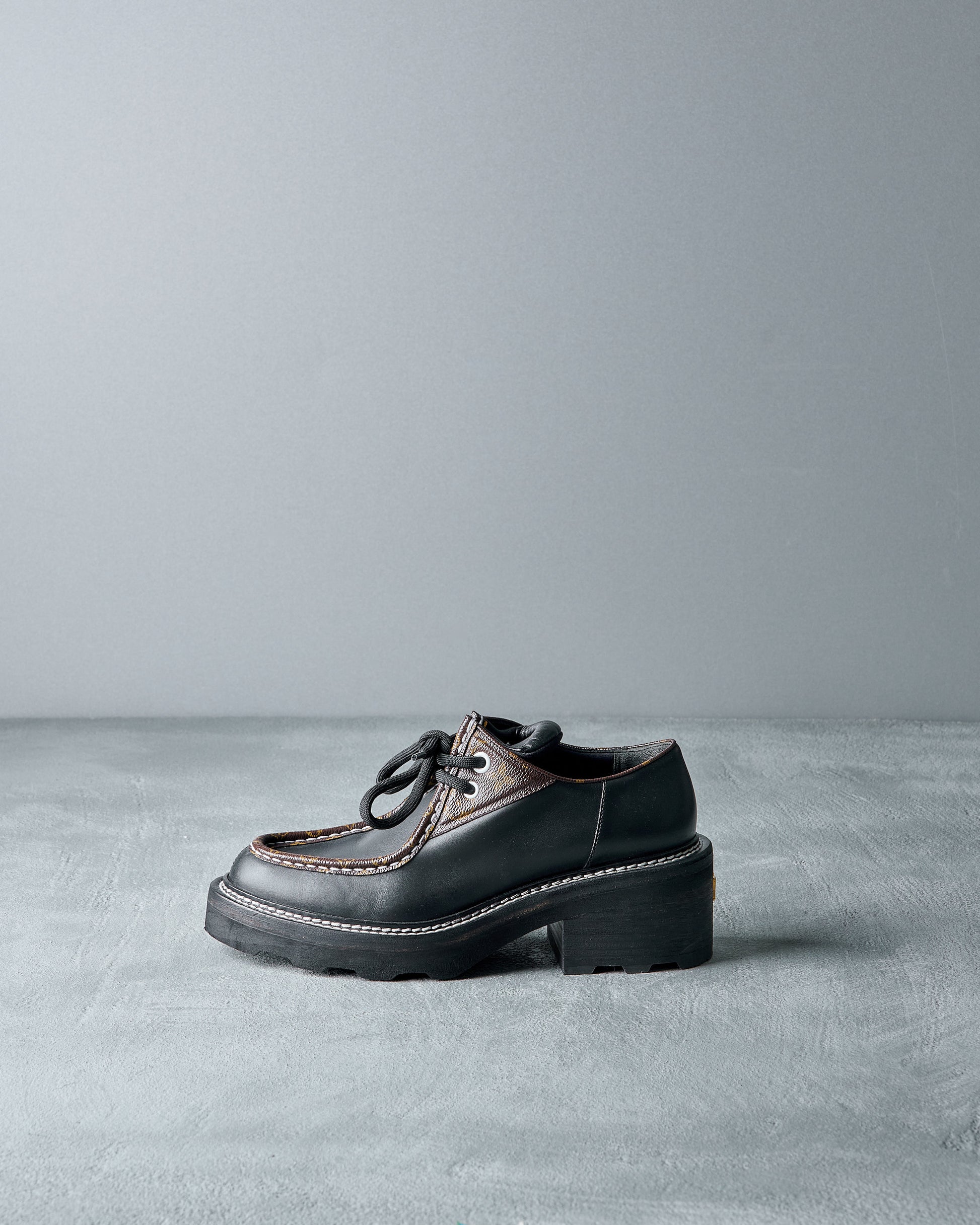 Black leather Louis Vuitton shoe with brown accents on a gray background