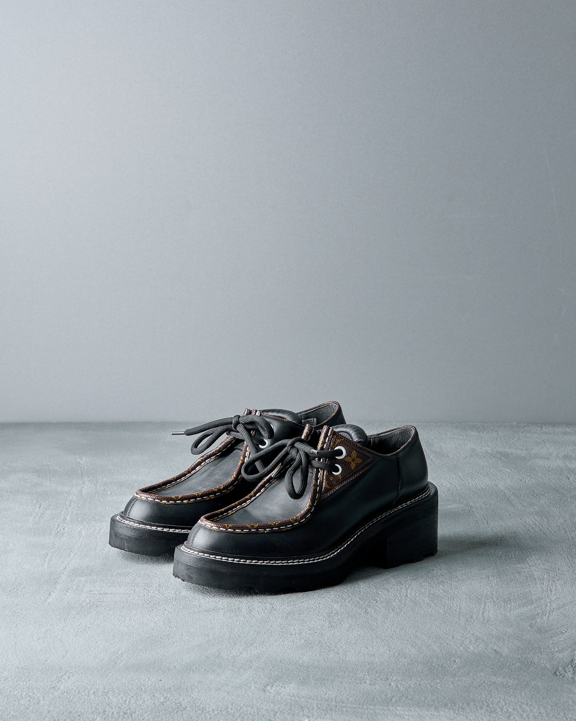 Pair of black leather Louis Vuitton shoes on a gray surface with a gray background