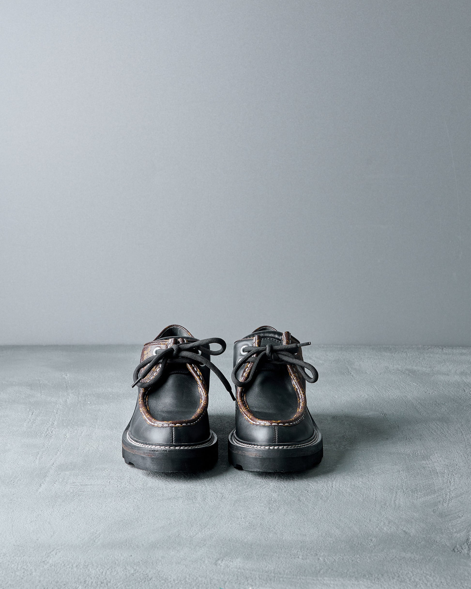 Pair of black leather Louis Vuitton shoes on a gray surface with a gray background