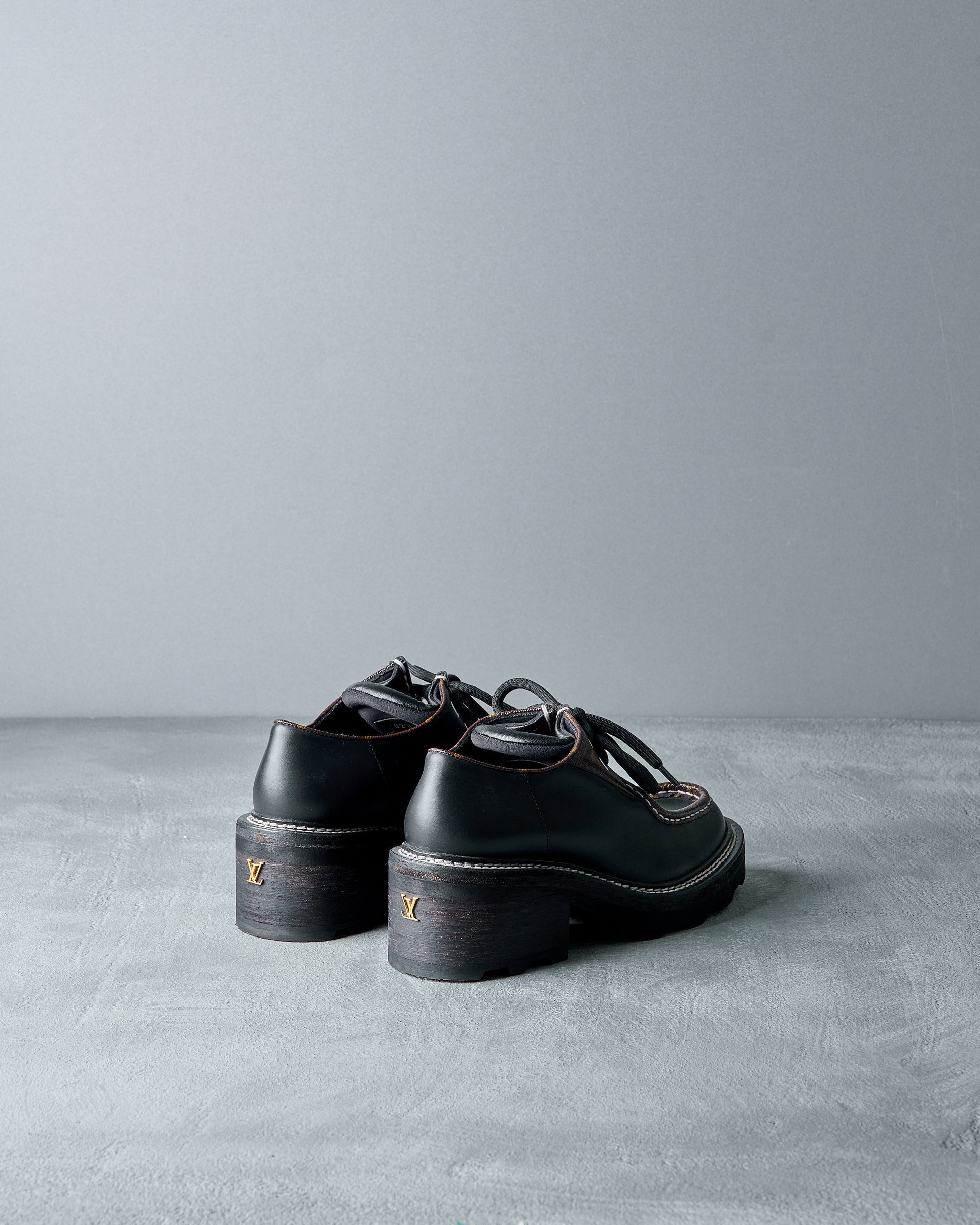 Pair of black Louis Vuitton shoes on a gray surface with a neutral background